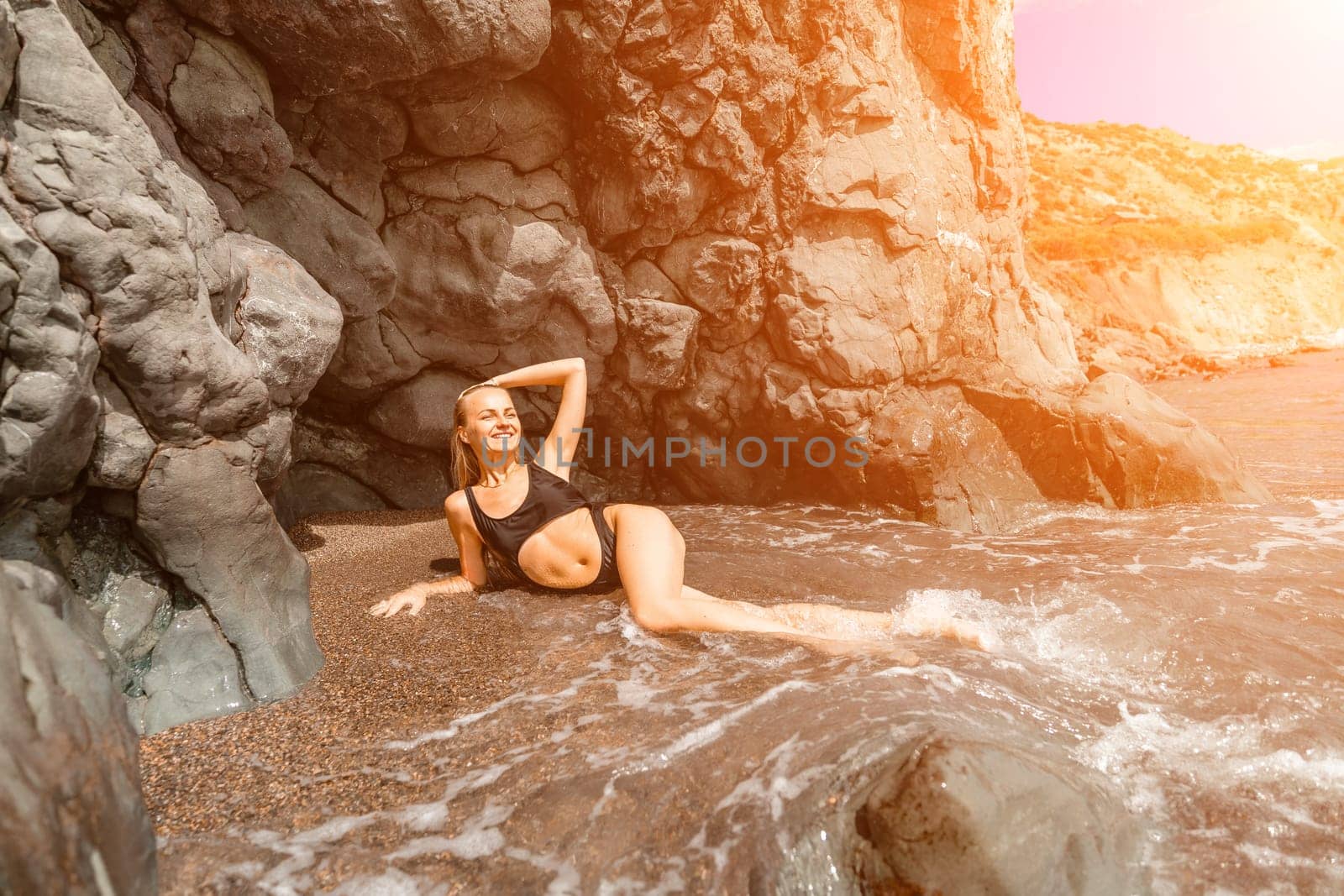 Woman travel sea. Attractive blonde woman in a black swimsuit enjoying the sea air on the seashore around the rocks. Travel and vacation concept. by Matiunina