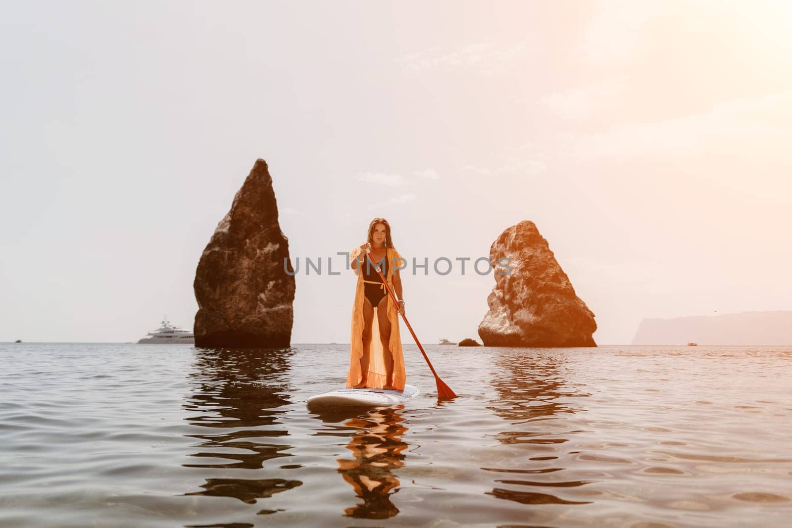 Close up shot of beautiful young caucasian woman with black hair and freckles looking at camera and smiling. Cute woman portrait in a pink bikini posing on a volcanic rock high above the sea