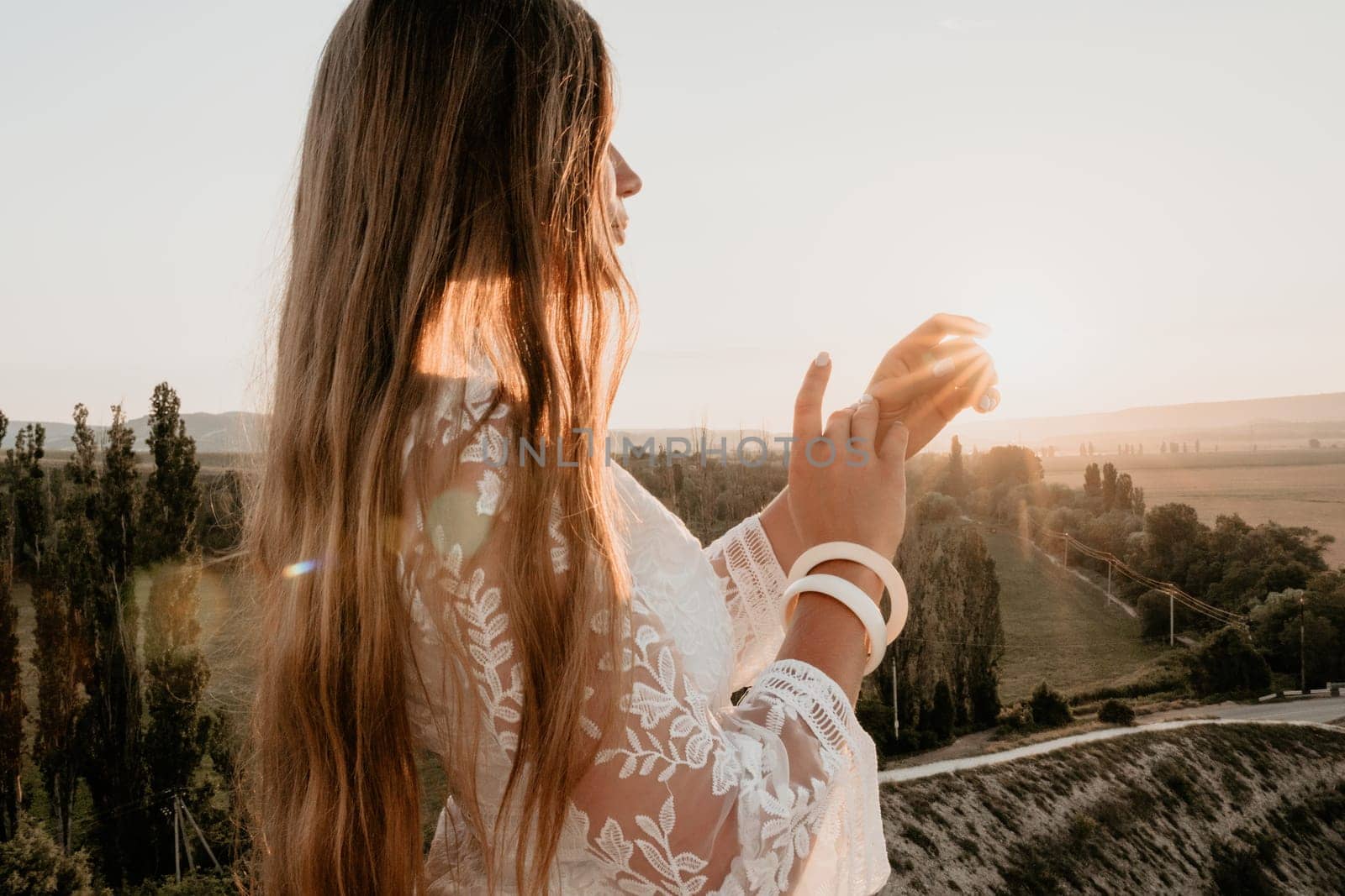 Romantic beautiful bride in white dress posing with sea and mountains in background. Stylish bride standing back on beautiful landscape of sea and mountains on sunset