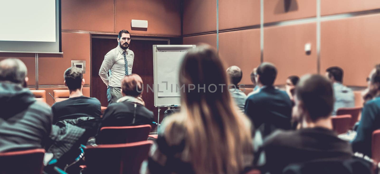 Public Speaker Giving a Talk at Business Meeting. Audience in the conference hall. Skilled coach answers questions of participants of business training. Business and Entrepreneurship concept.