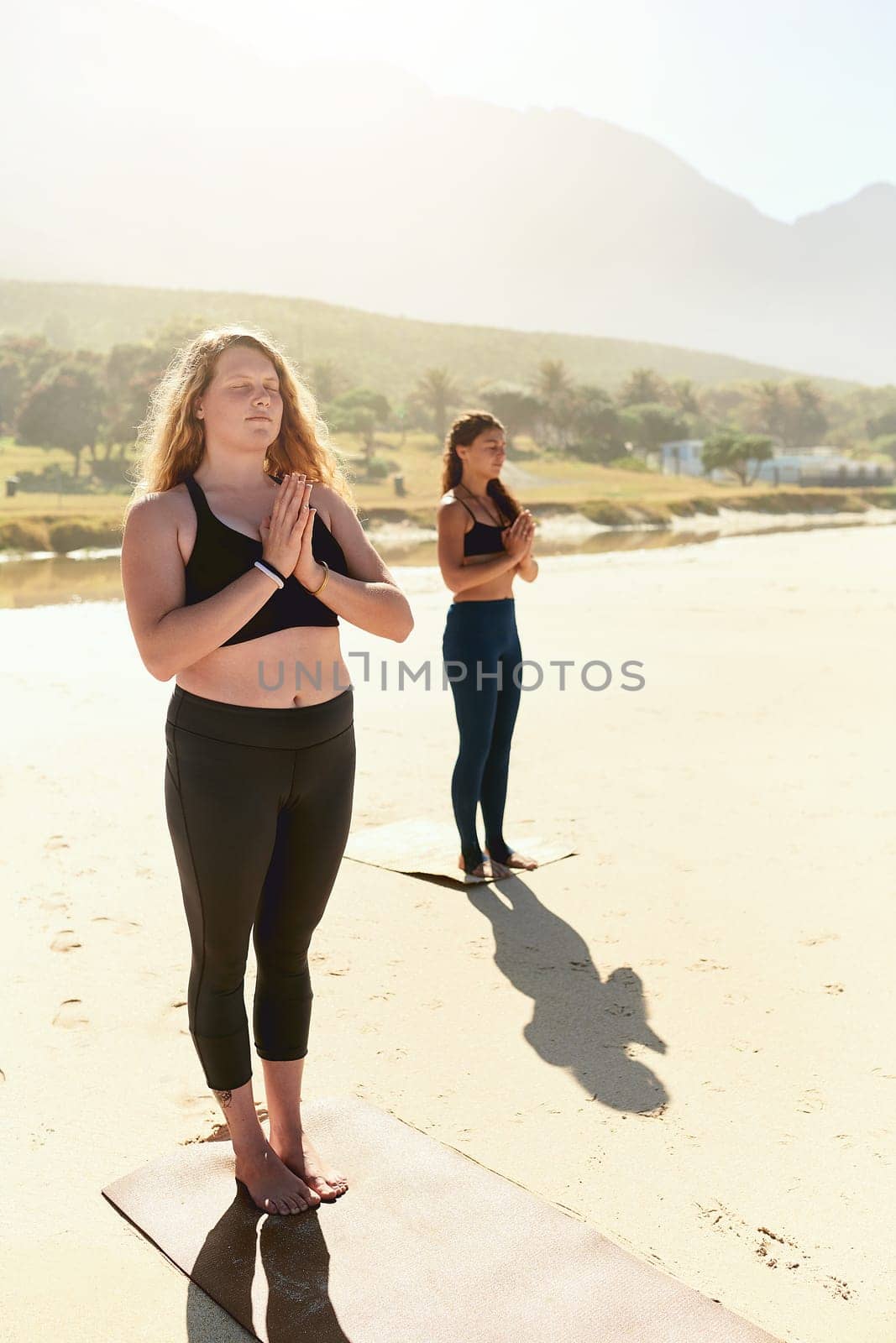 Yoga helps you maintain, recover or improve your health. two young women practising yoga on the beach. by YuriArcurs