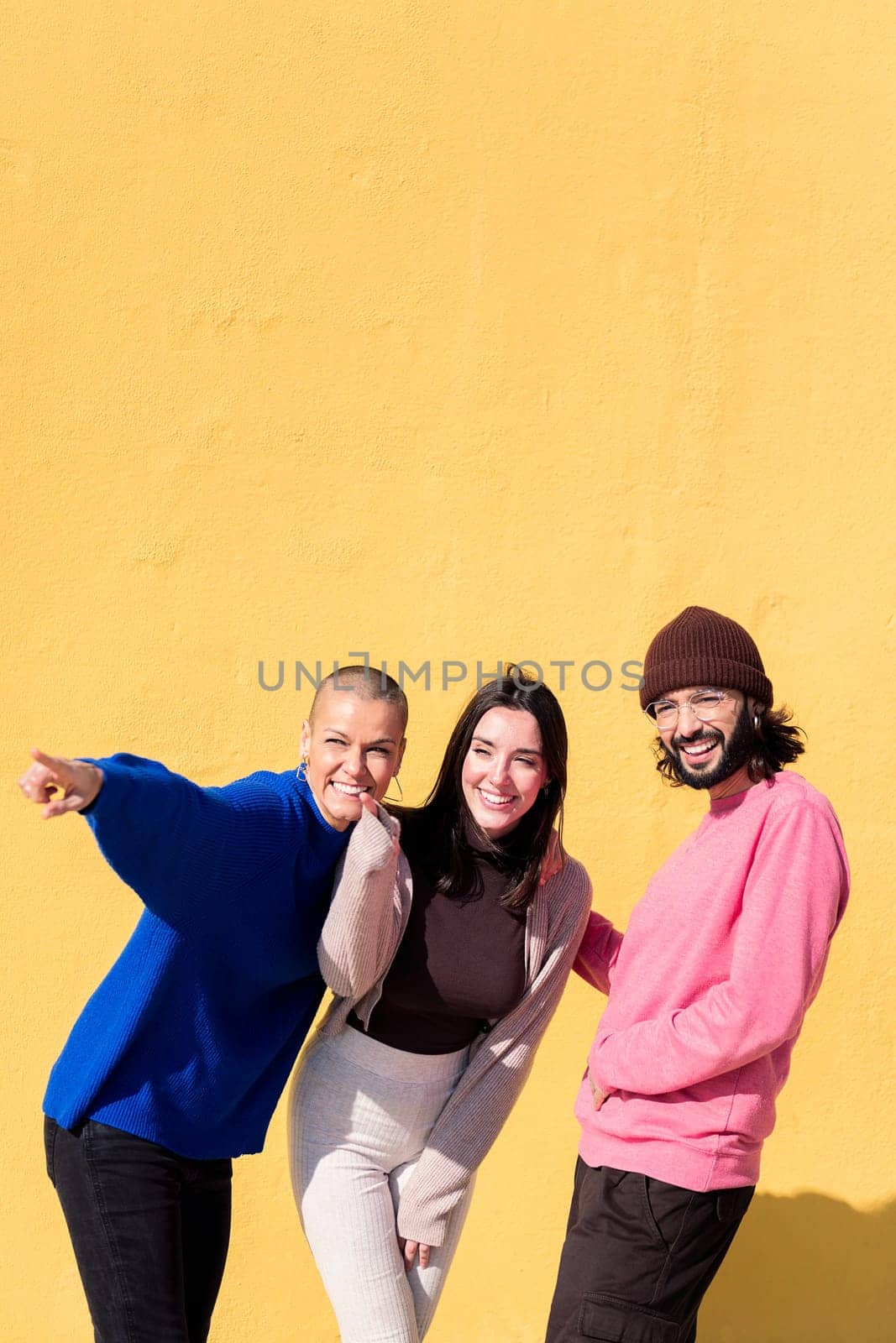 joyful young people pointing and having fun together on yellow background, concept of friendship and happiness, copy space for text