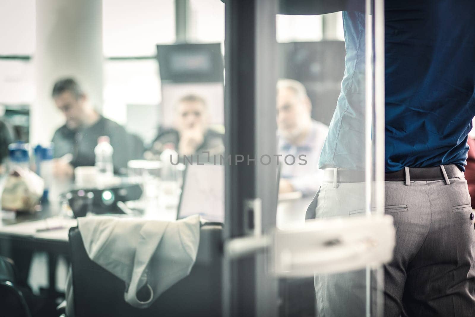 Business man making a presentation at office. Business executive delivering a presentation to his colleagues during meeting or in-house business training. View through glass.