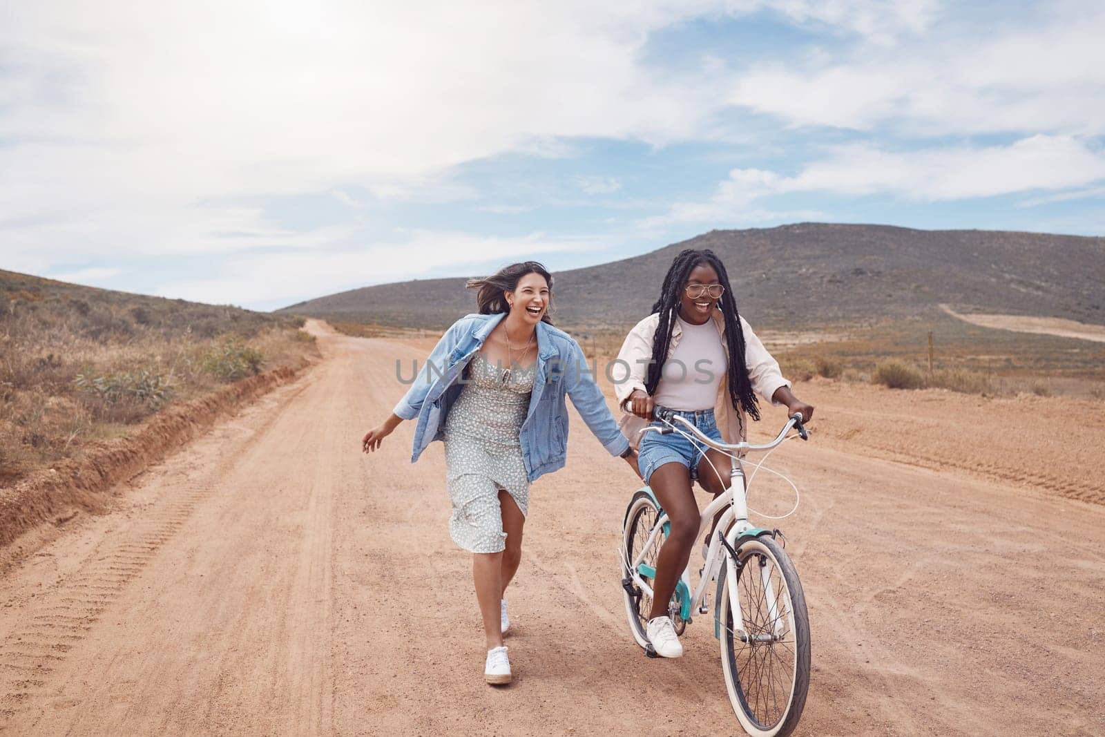 Bike ride, girl friends and road trip fun of women outdoor on a desert path on summer vacation. Cycling, running and freedom of young people together with bicycle transportation feeling free.