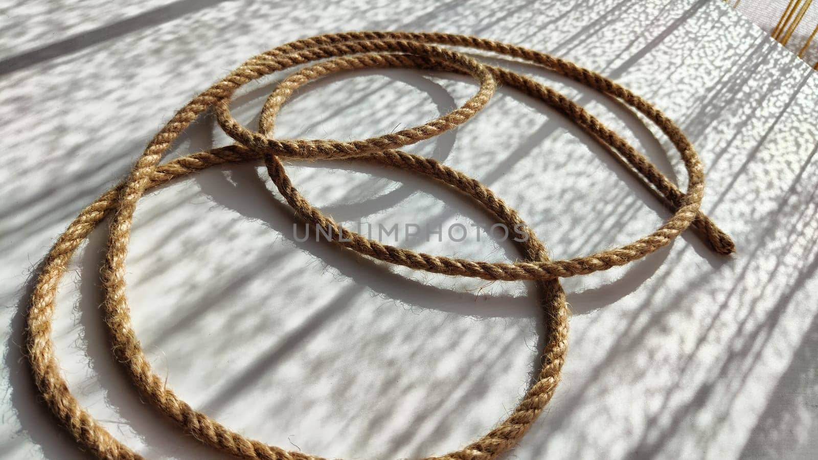 Jute twisted rope lying on a white surface with shadows from the sun. Abstract background, texture, pattern, frame by keleny