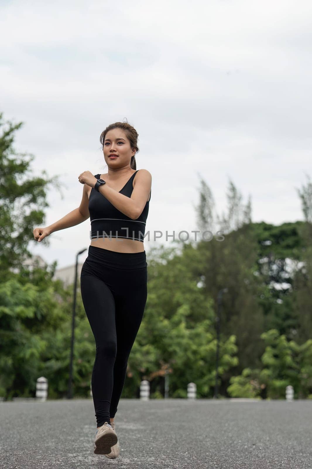 Happy woman wearing sportswear jogging in the park. Young beautiful asian female in sports bra running outdoor. Workout exercise in the morning. Healthy and active lifestyle concept.