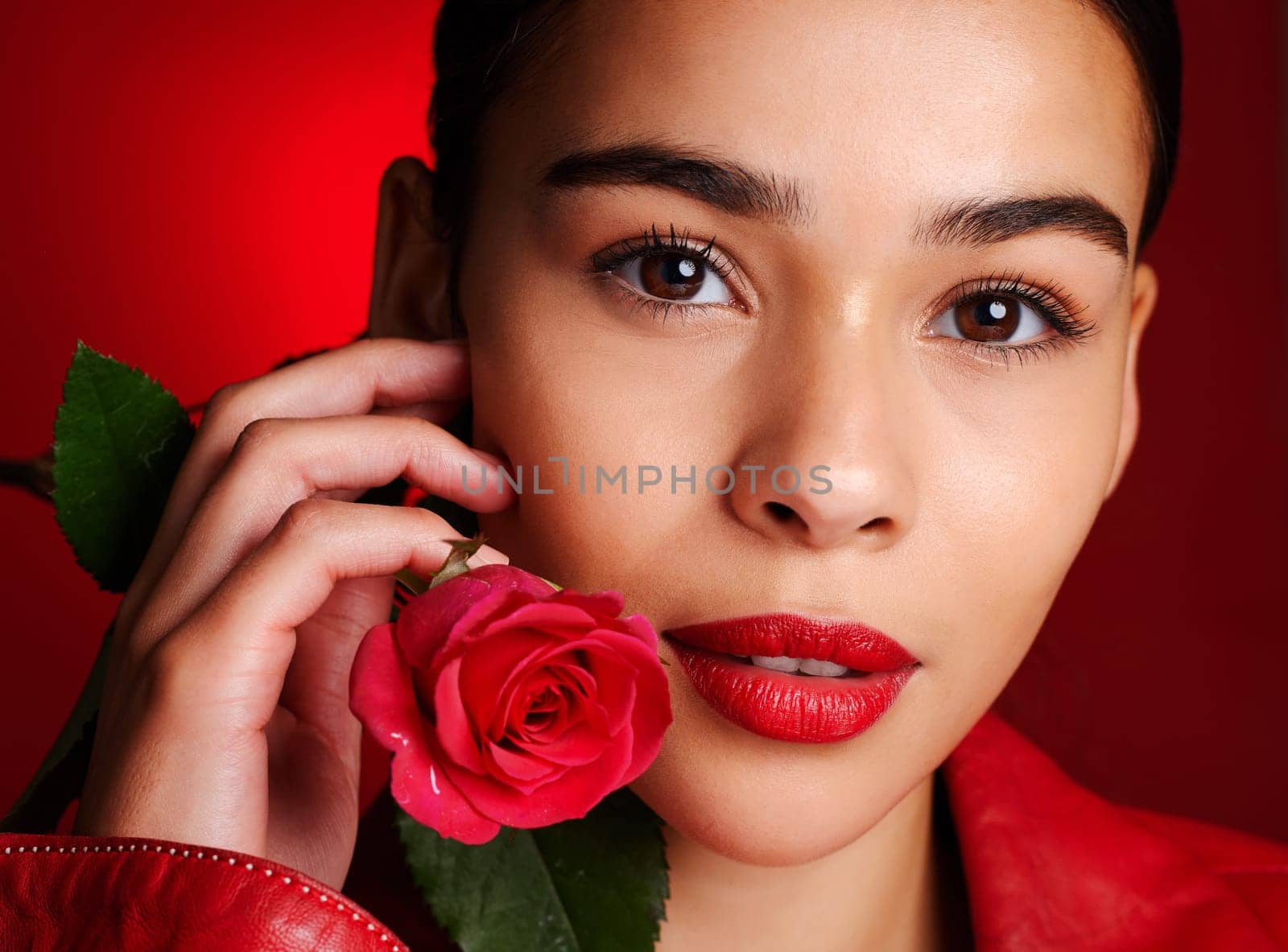 Portrait, beauty and red rose with a model woman holding a flower in studio on a wall background for valentines day. Face, romance and love with an attractive young female posing to promote dating by YuriArcurs