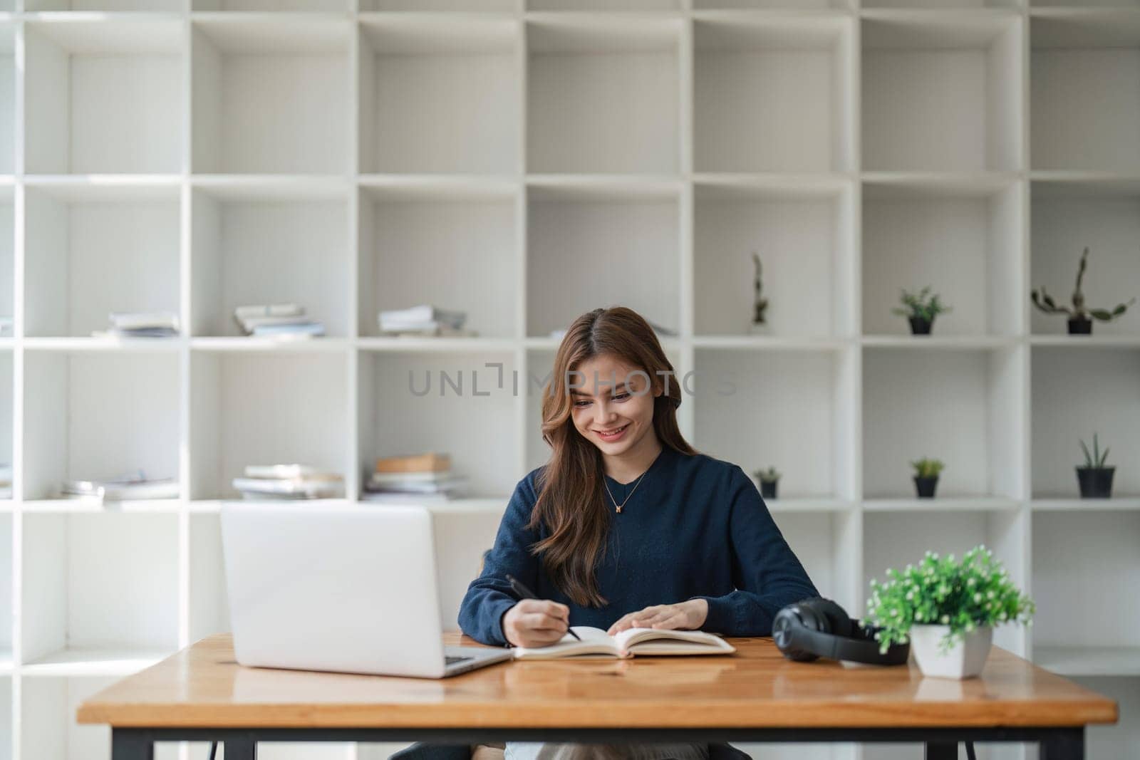 girl using laptop at home looking at write or take notes in a notebook. Young woman having virtual meeting online chat video call conference. Work learning from home by nateemee