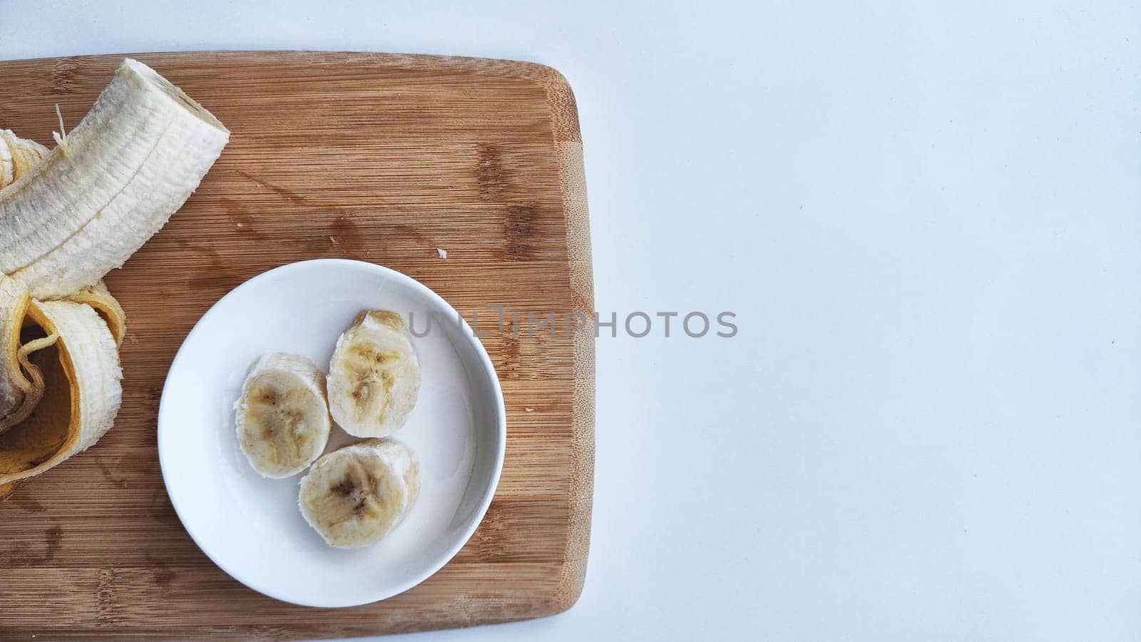 Banana with open panel on wooden board and sliced round pieces on the plate on white background. Ripe banana with peel and cooking. Delicious sweet fruit dessert. Close up