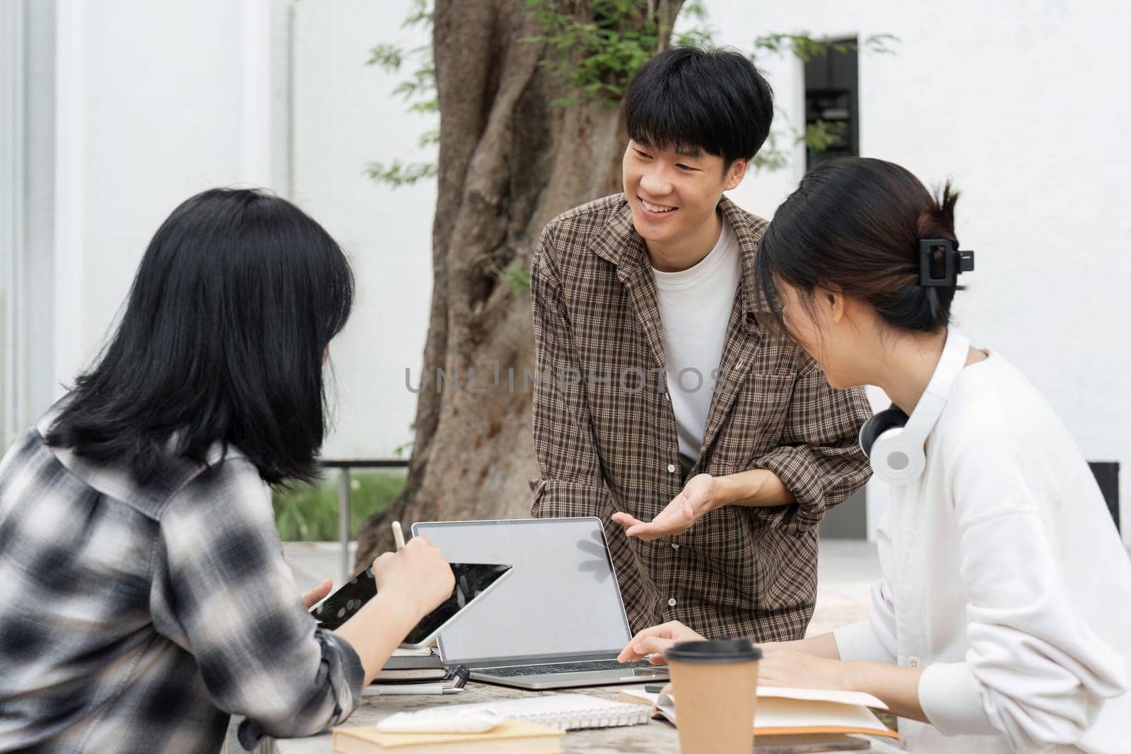 Group of happy students checking results on laptop and tablet while sitting on college campus, concept of education, technology and project work discussion.