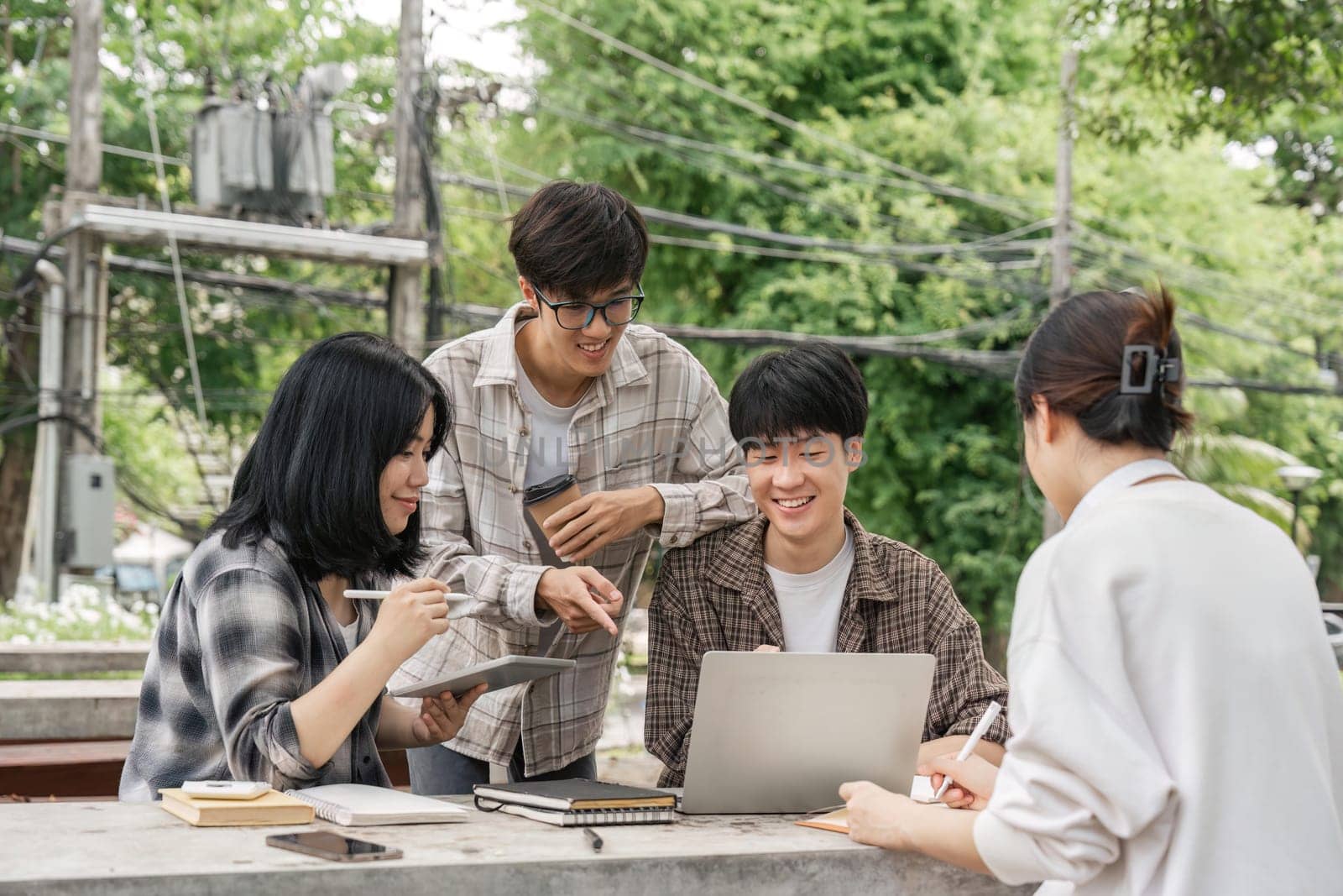 University students sitting together at table with books and laptop and tablet. Happy young people doing group study in university by nateemee