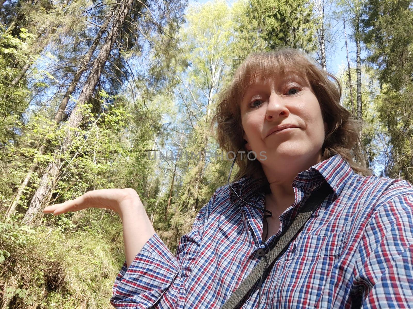 The blonde girl tourist takes selfie in nature in the forest on a hike or trip. The pretty woman poses while traveling in the summer, spring, or fall