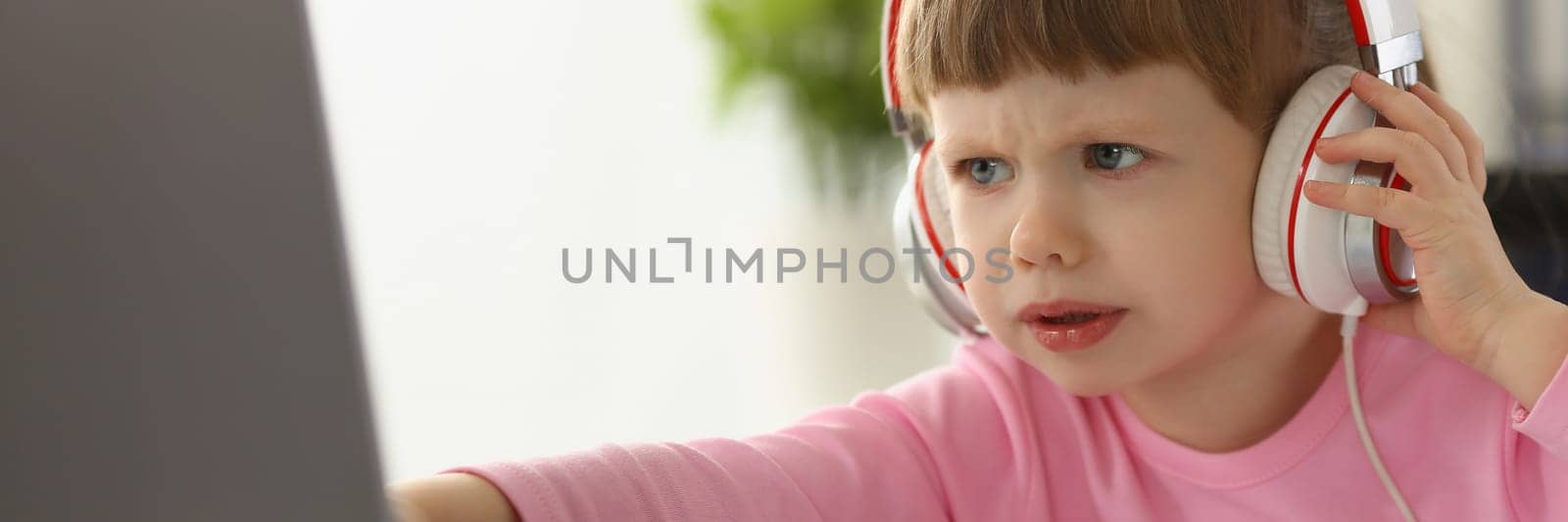 Little girl child in headphones in front of laptop by kuprevich