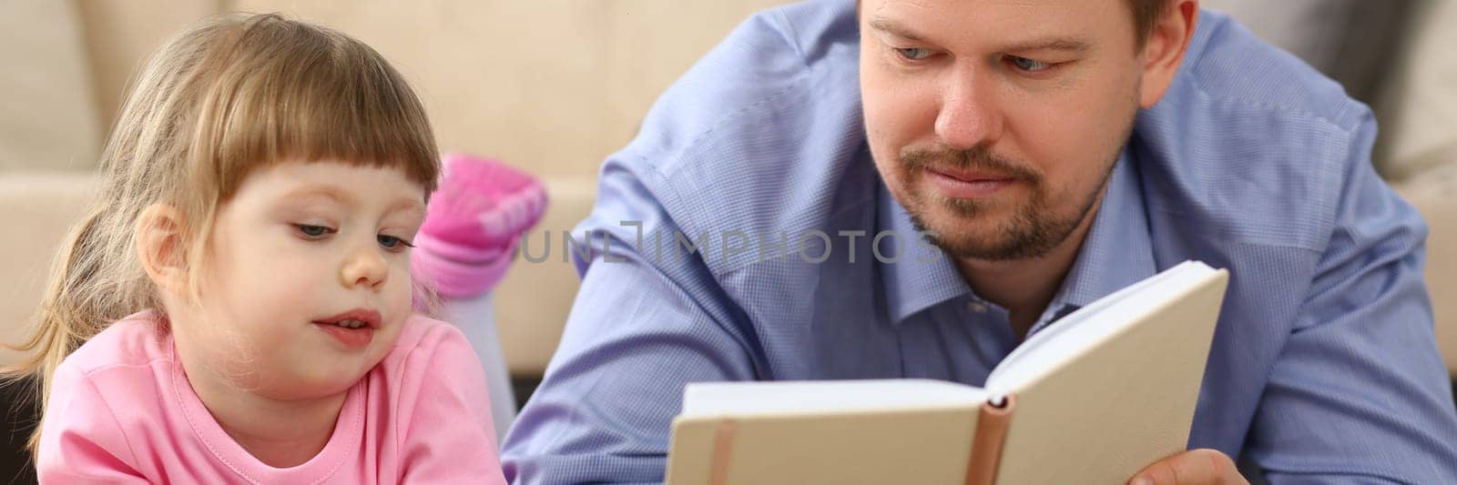 Dad reads a book to daughter holding smartphone lying on floor by kuprevich