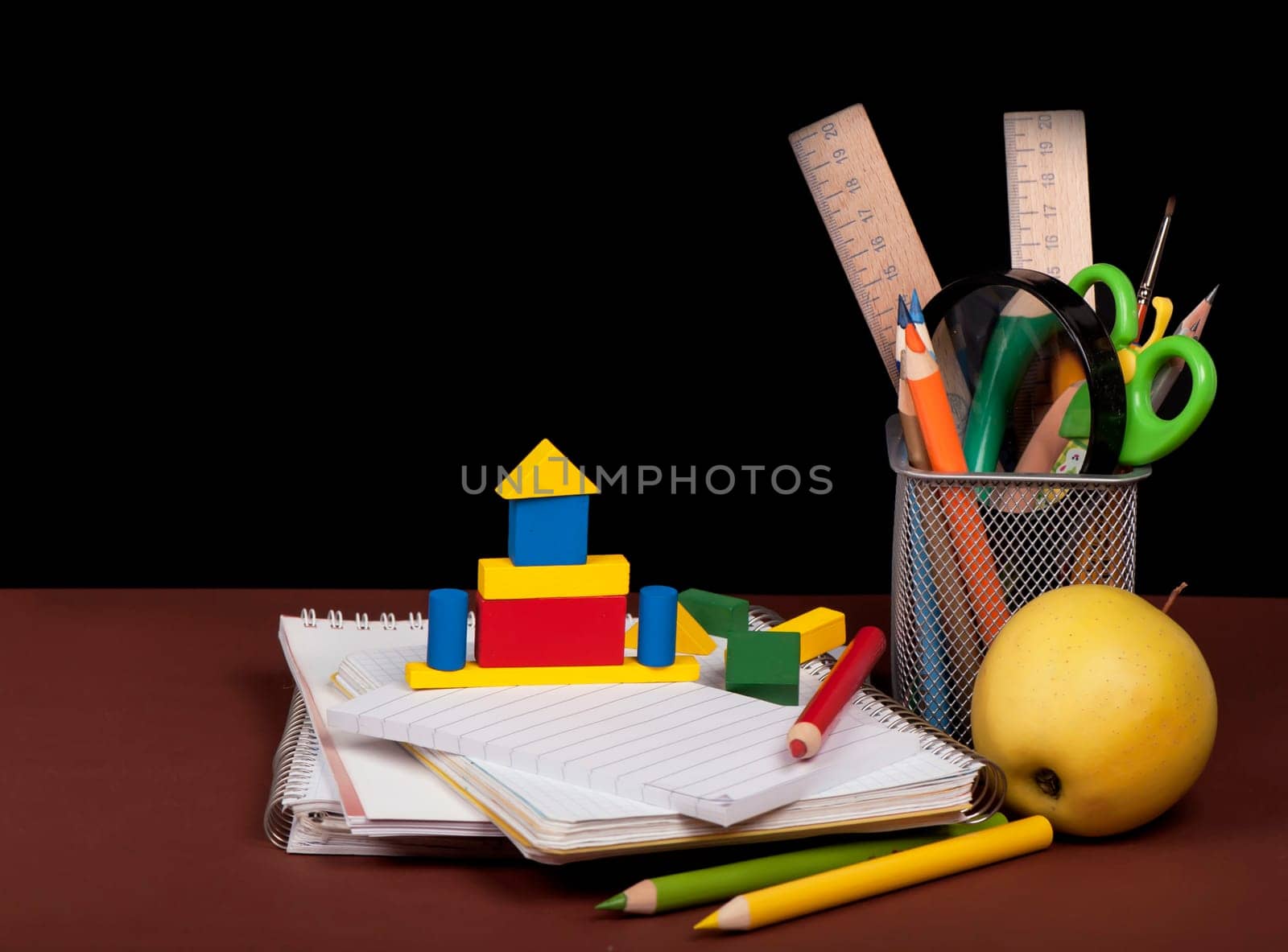 Magnifying glass, scissors, colored paper, textbooks, Apple, cubes, board, pencils, opened empty notebook against a dark background by aprilphoto