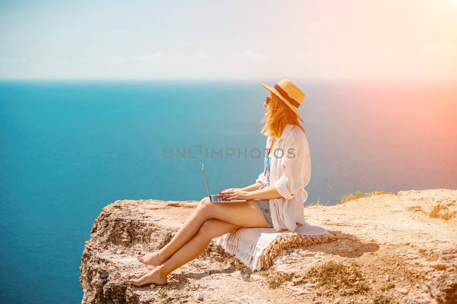 Freelance woman working on a laptop by the sea, typing away on the keyboard while enjoying the beautiful view, highlighting the idea of remote work. by Matiunina