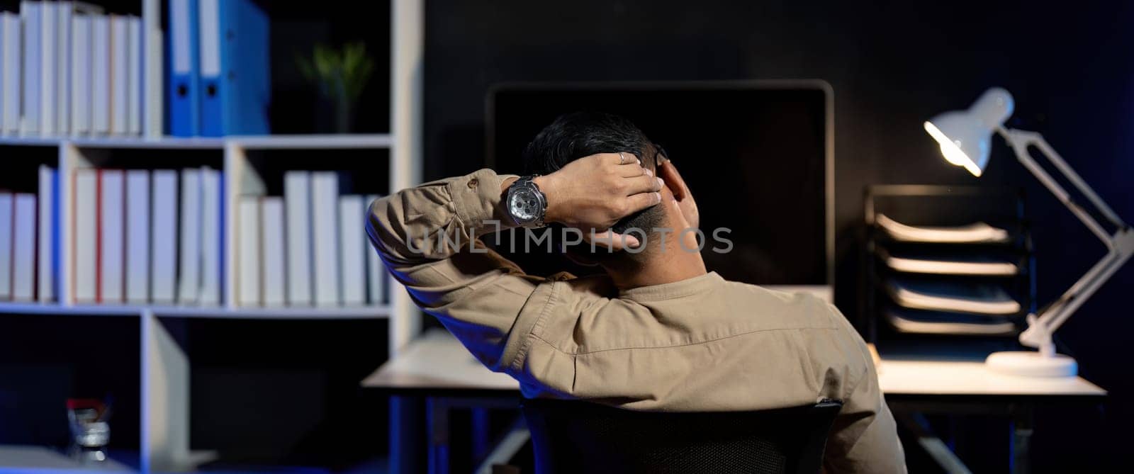 Overworked young Asian office employee working on laptop computer overtime in office at night.