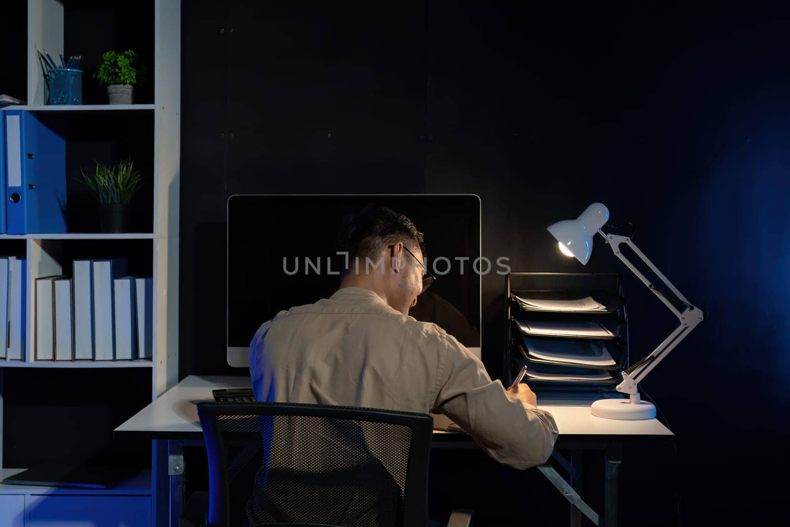 Overworked young Asian office employee working on laptop computer overtime in office at night.