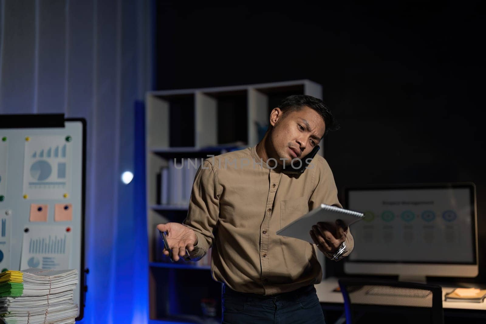 Overworked young Asian office employee working on laptop computer overtime in office at night.