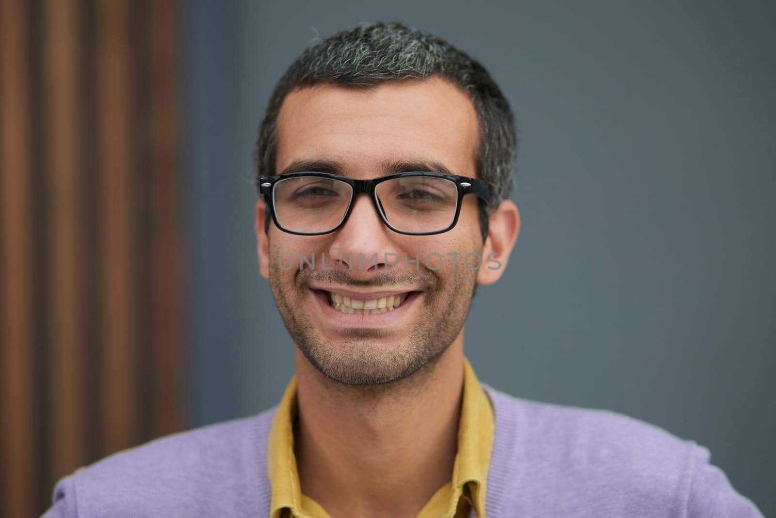 Close-up of a handsome adult man, wearing a lilac t-shirt, smiling happily, standing in the office
