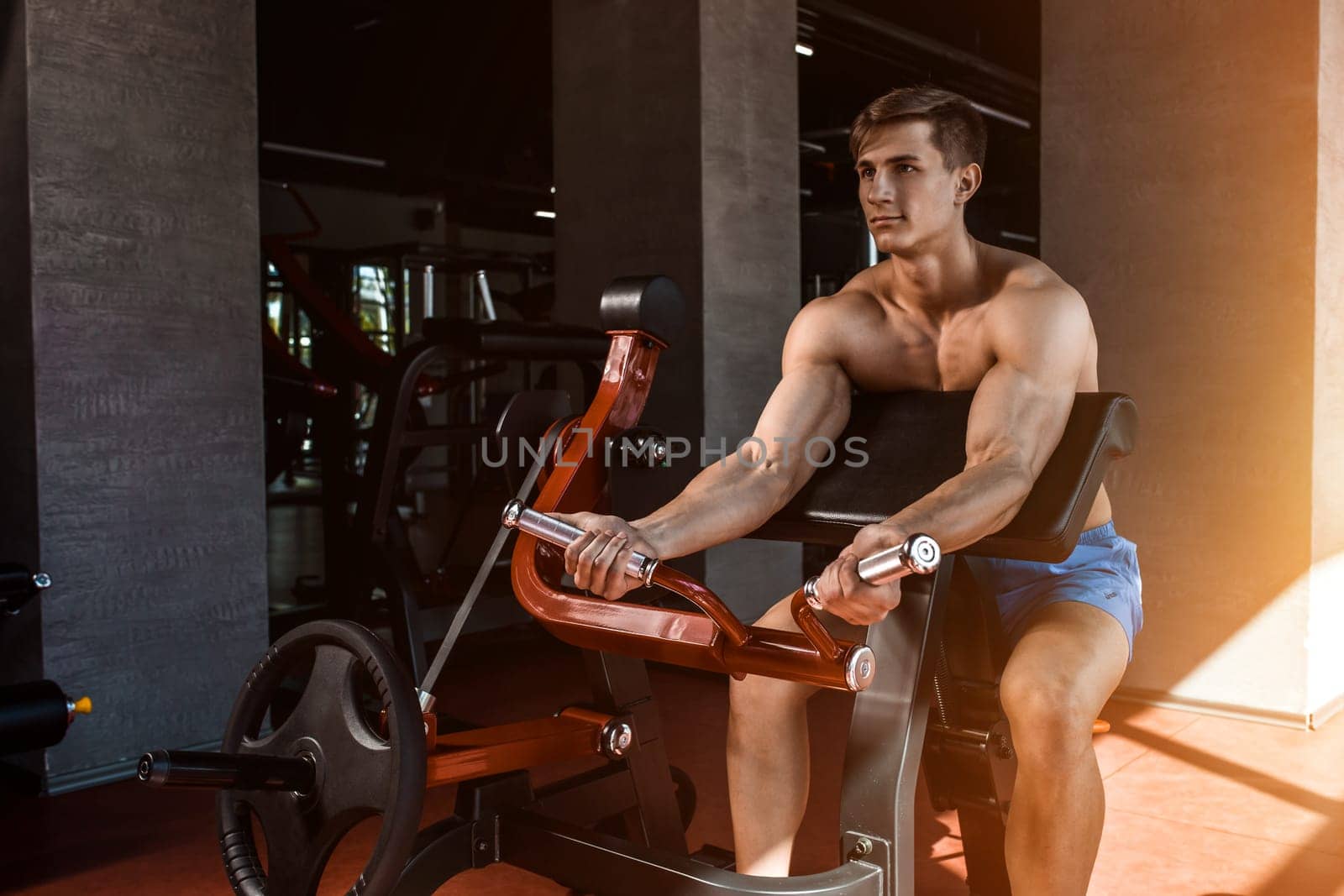 Tense muscles of hands under load. Man doing exercise for biceps in the gym. Work on tell muscles on the simulator. Photos for sporting magazines, posters and websites. sun flare