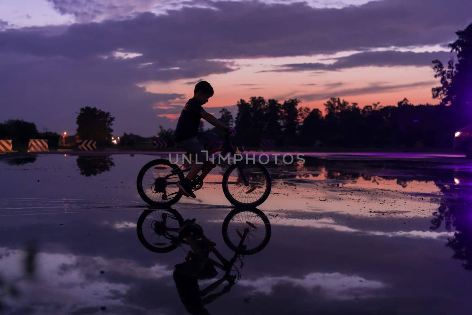 Lonely children silhouette on bike, boy riding bicycle on reflective water. Background beautiful sunset. by dotshock
