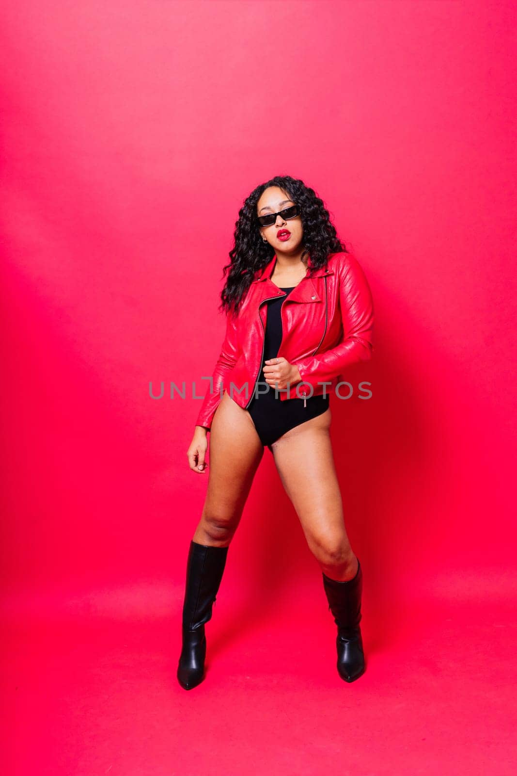 African American curvy female in black bodysuit and jacket on red and white background in a studio