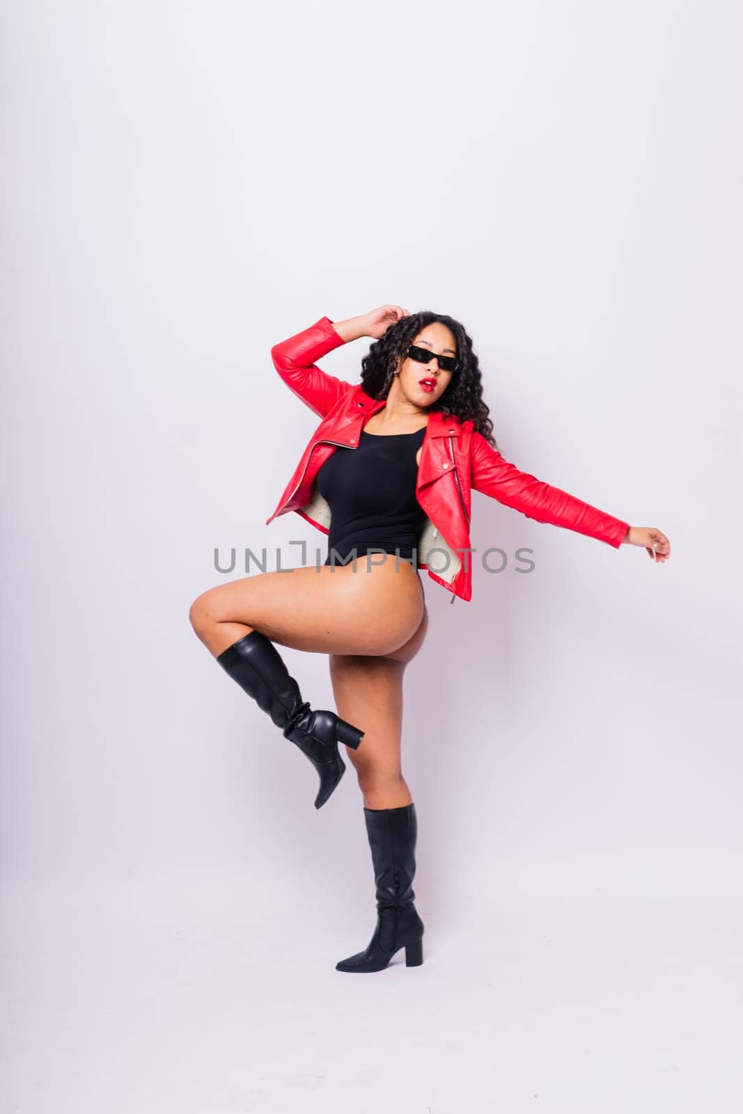 African American curvy female in black bodysuit and jacket on red and white background in a studio