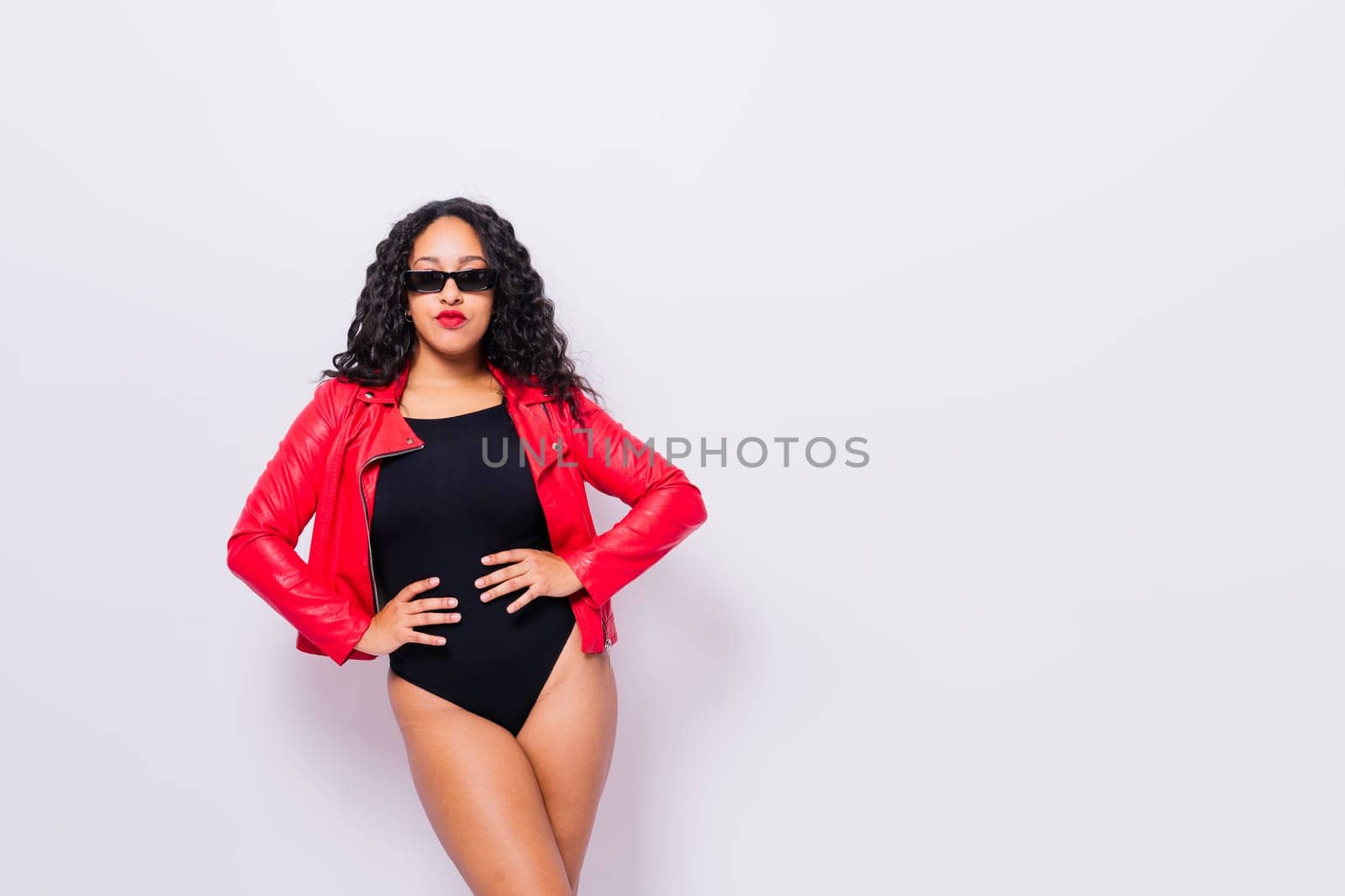 African American curvy female in black bodysuit and jacket on red and white background in a studio