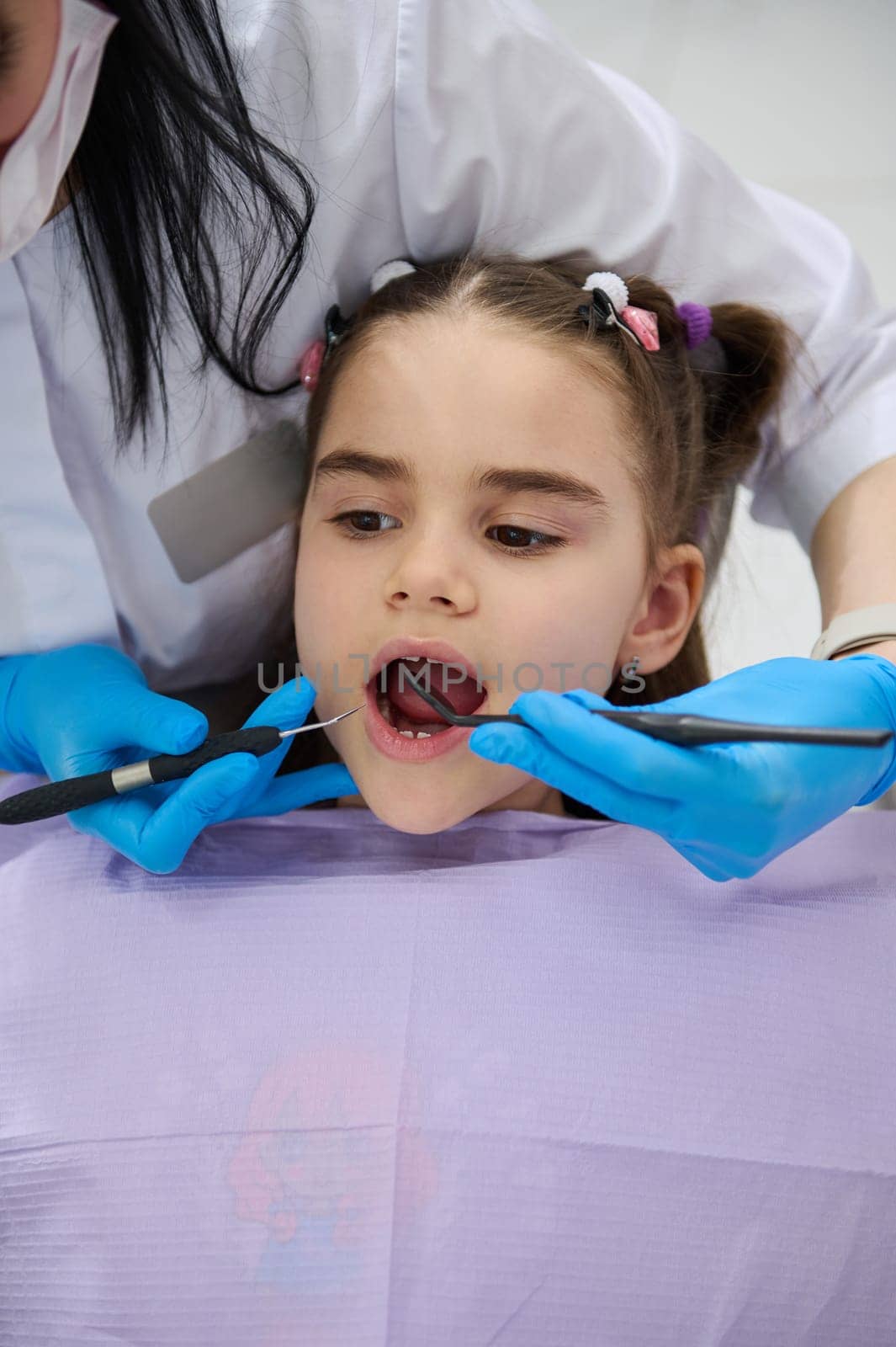 Close-up of little child girl in dentist's chair, being examined by a doctor dentist, curing caries in dentistry clinic by artgf