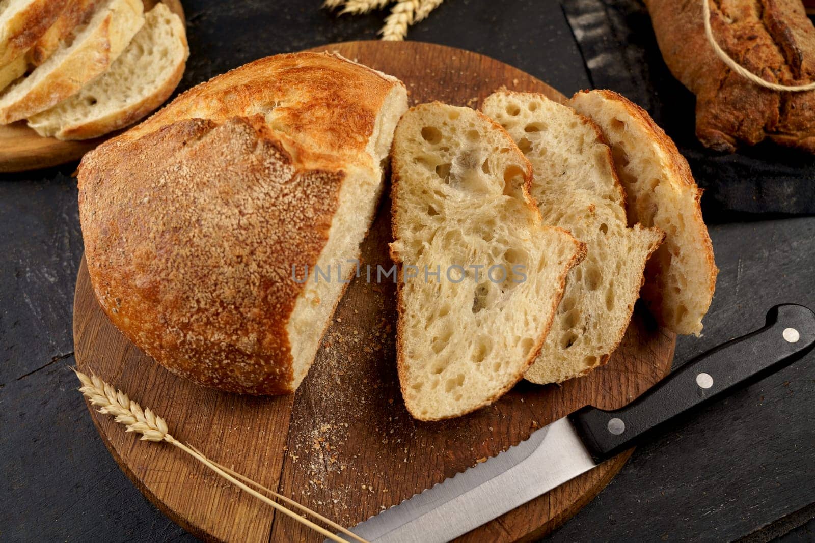 Fresh bread slice and cutting knife on rustic table Round loaf of freshly baked sourdough bread with knife on cutting board. Concept of homemade bread, natural farm products, domestic production. Healthy and tasty organic food.