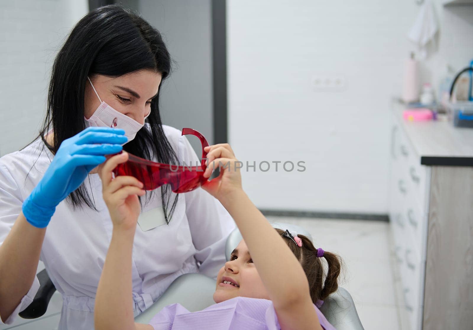 Pediatric dentistry. Dental practice. Pleasant female dentist doctor talking to a little patient before dental check up. Oral health and hygiene. The concept of baby teeth treatment. Caries prevention