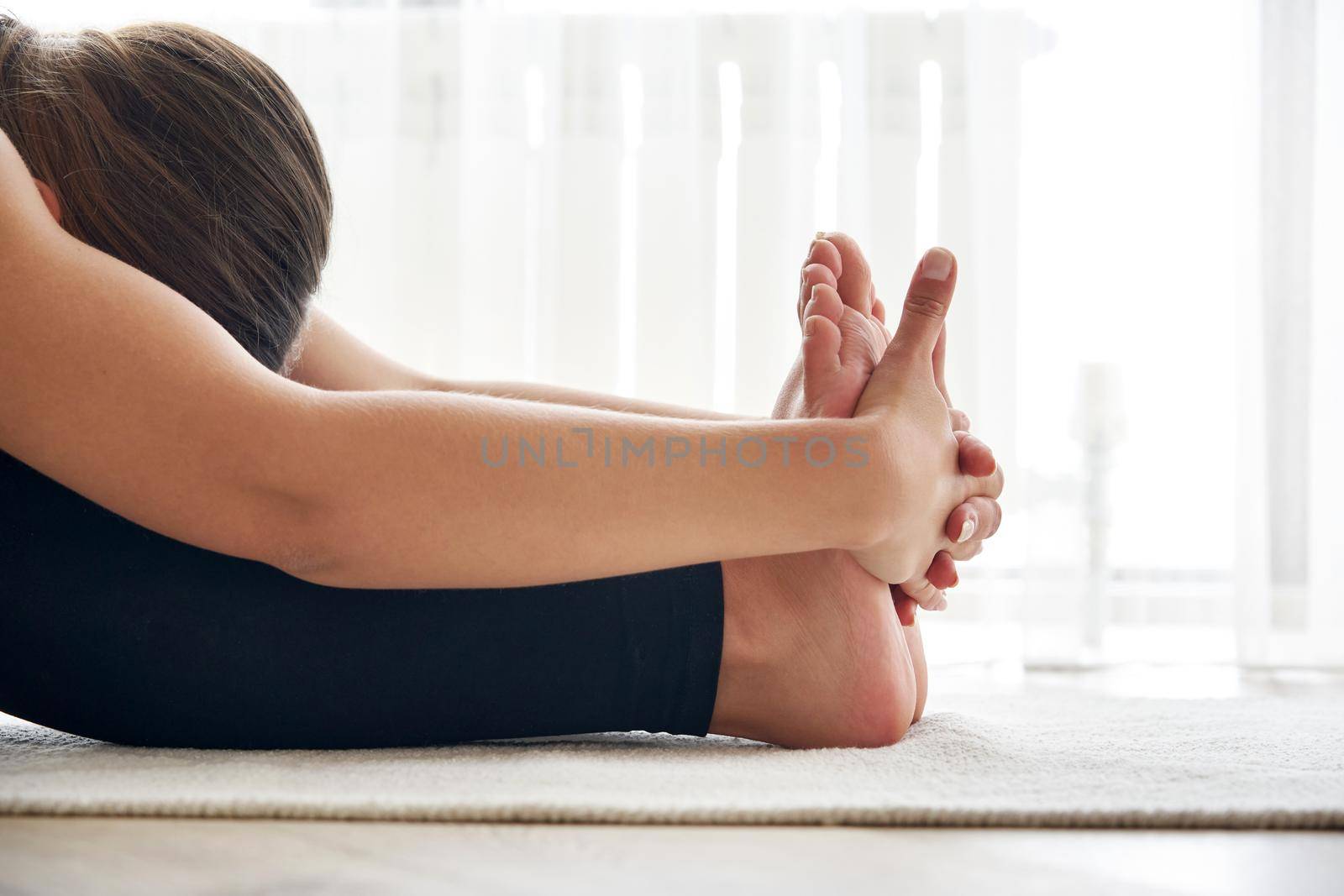 Cropped view of young woman practicing yoga, sitting in Seated forward bend exercise, paschimottanasana pose by Mariakray