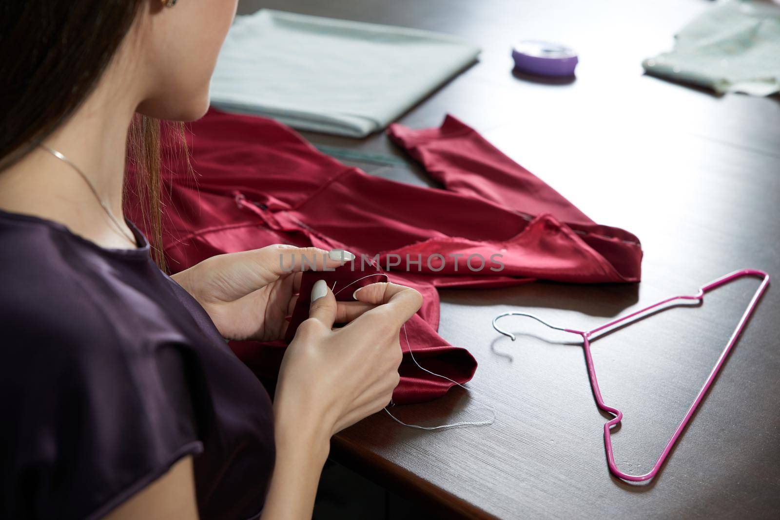 Beautiful young dressmaker in workroom sewing red dress