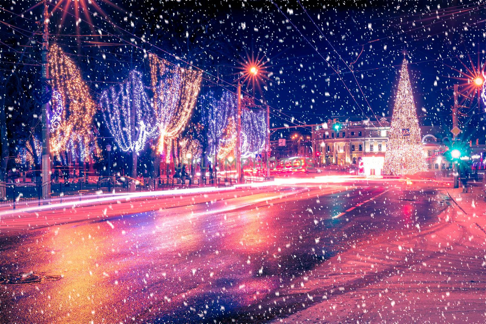 Night city with Christmas decorations, spruce and traces of headlights of moving cars, reflected in the wet road in a snowfall. by Eugene_Yemelyanov