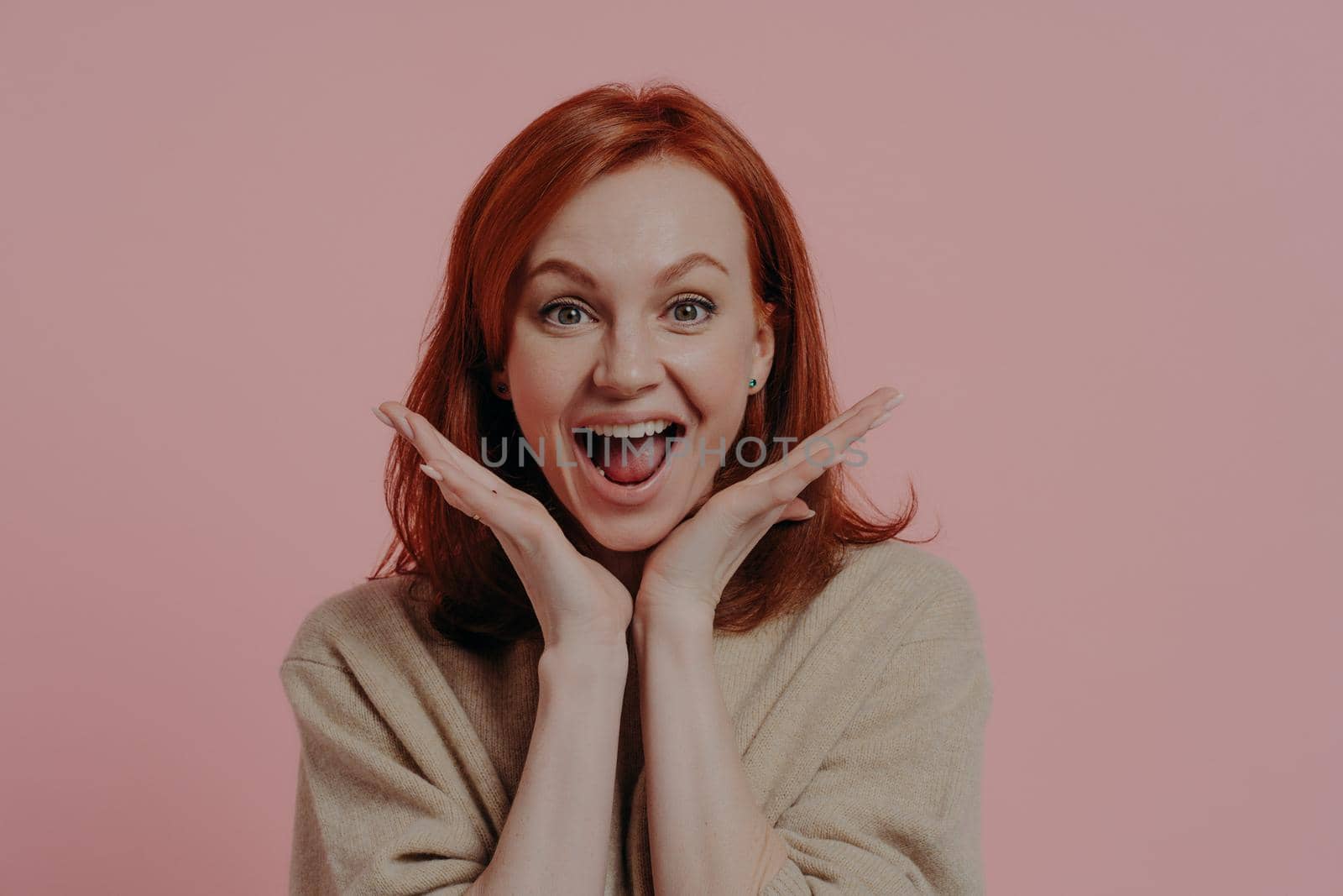 Wow! Portrait of young surprised beautiful ginger woman spreading palms near face and keeping mouth open from excitement, isolated over studio background, dressed in casual clothes. Surprise concept