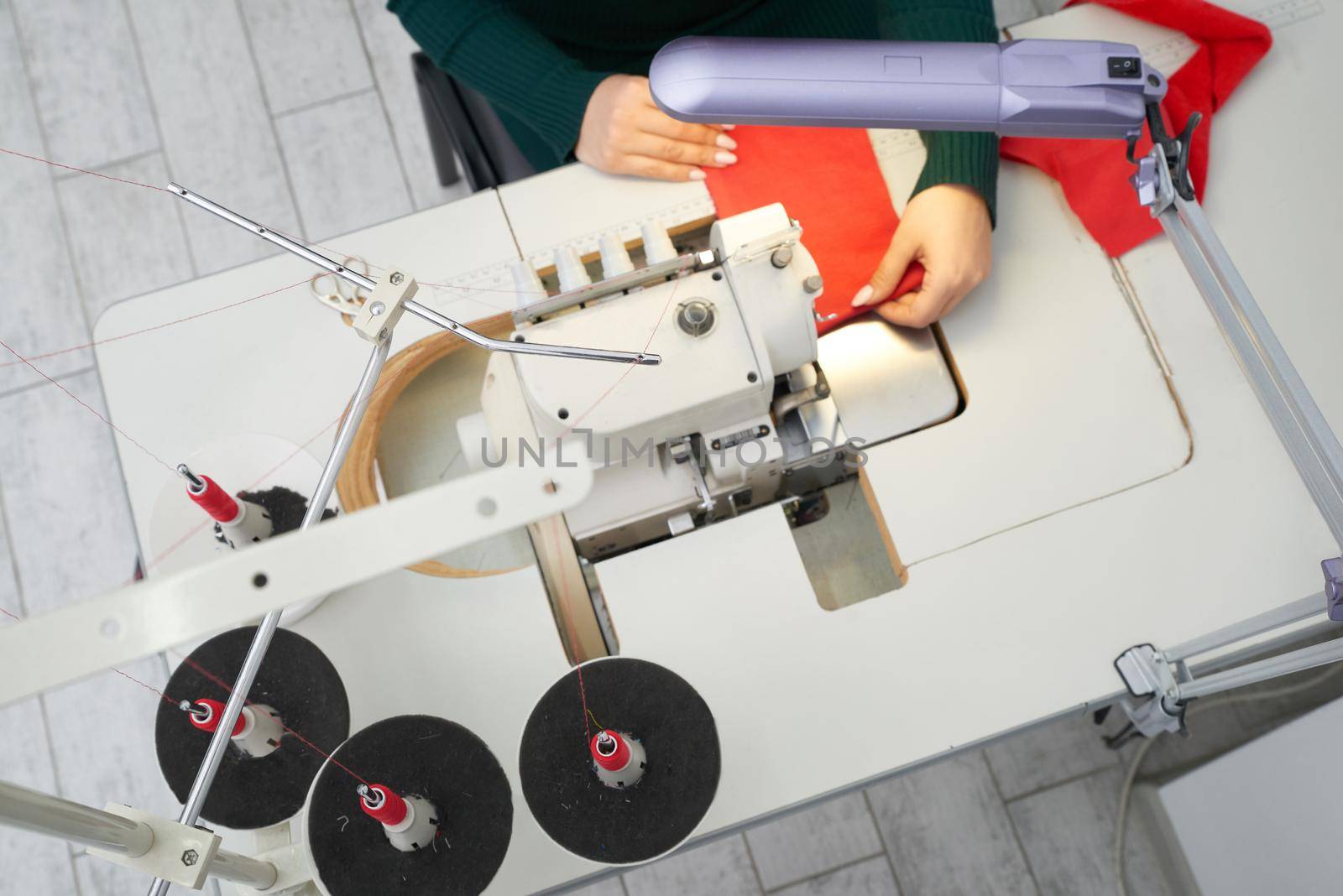 Young woman using professional overlock sewing machine in workshop. Equipment for edging, hemming or seaming clothes at tailors shop