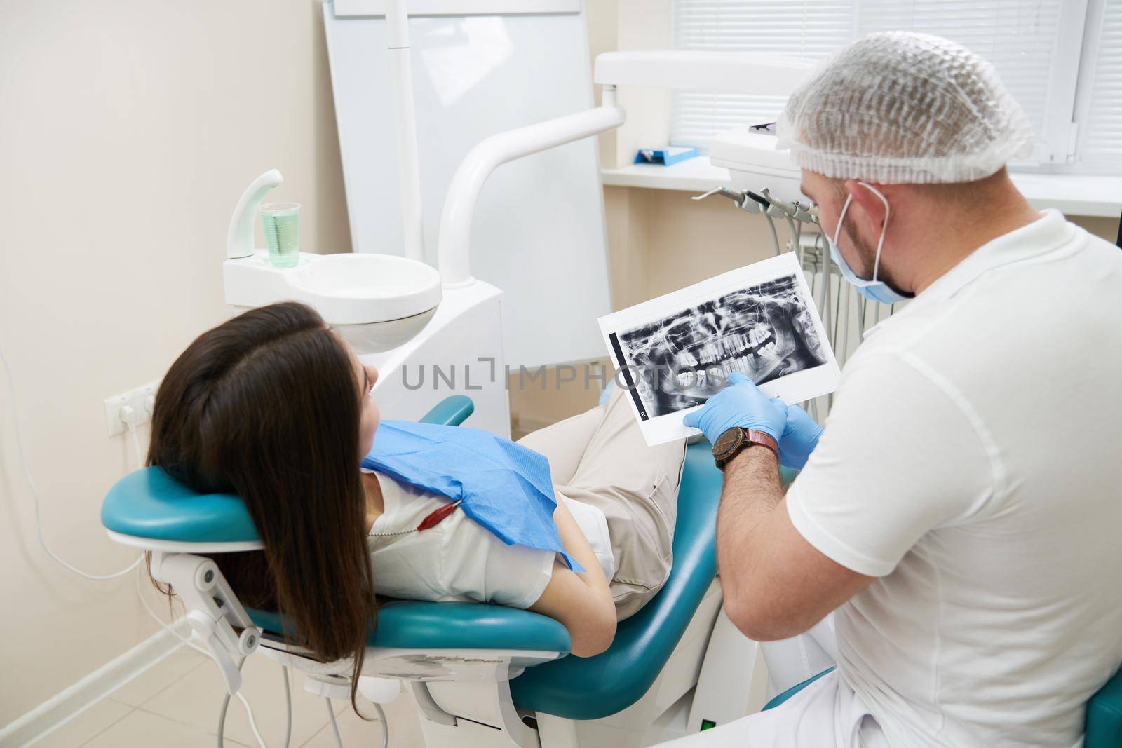 Professional doctor shows to the patient picture of teeth in his medical dental office. Doctor wearing medical clothing.