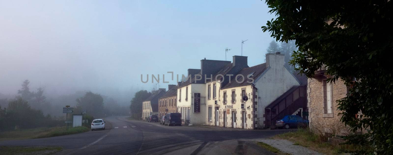 poullaouen, france, 12 august 2021: village with typical breton houses along road in central brittany on early foggy morning