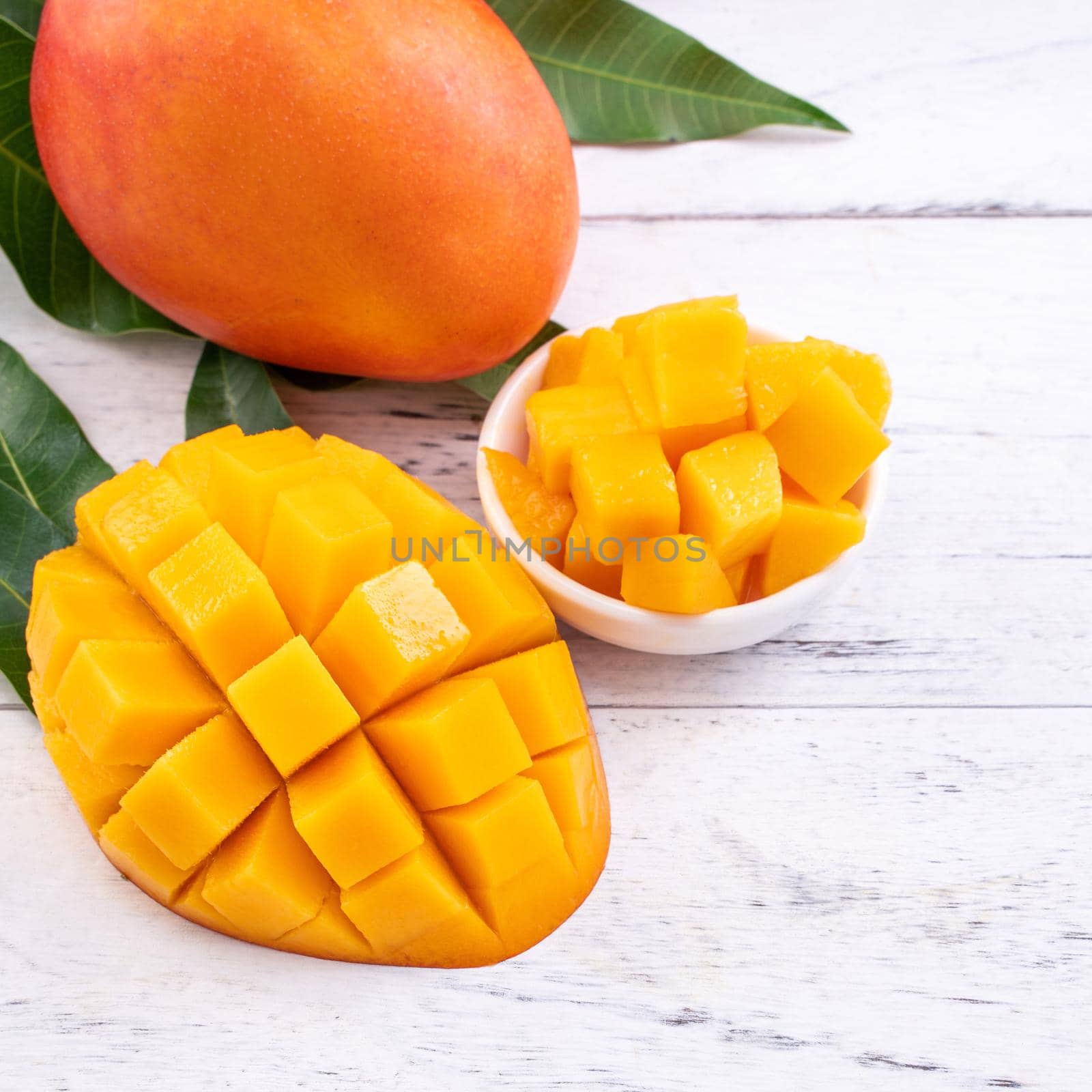 Fresh mango,beautiful chopped fruit with green leaves on bright wooden table background. Tropical fruit design concept, close up, copy space.