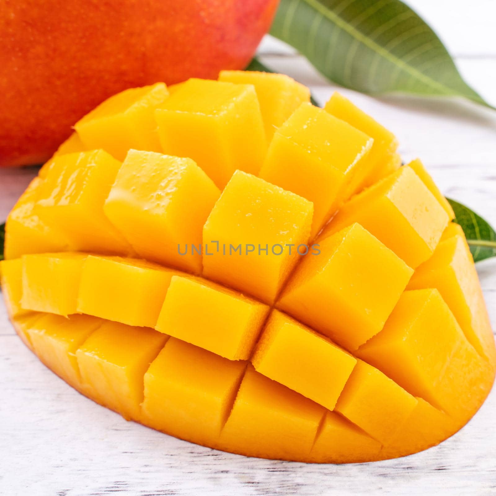 Fresh mango,beautiful chopped fruit with green leaves on bright wooden table background. Tropical fruit design concept, close up, copy space.