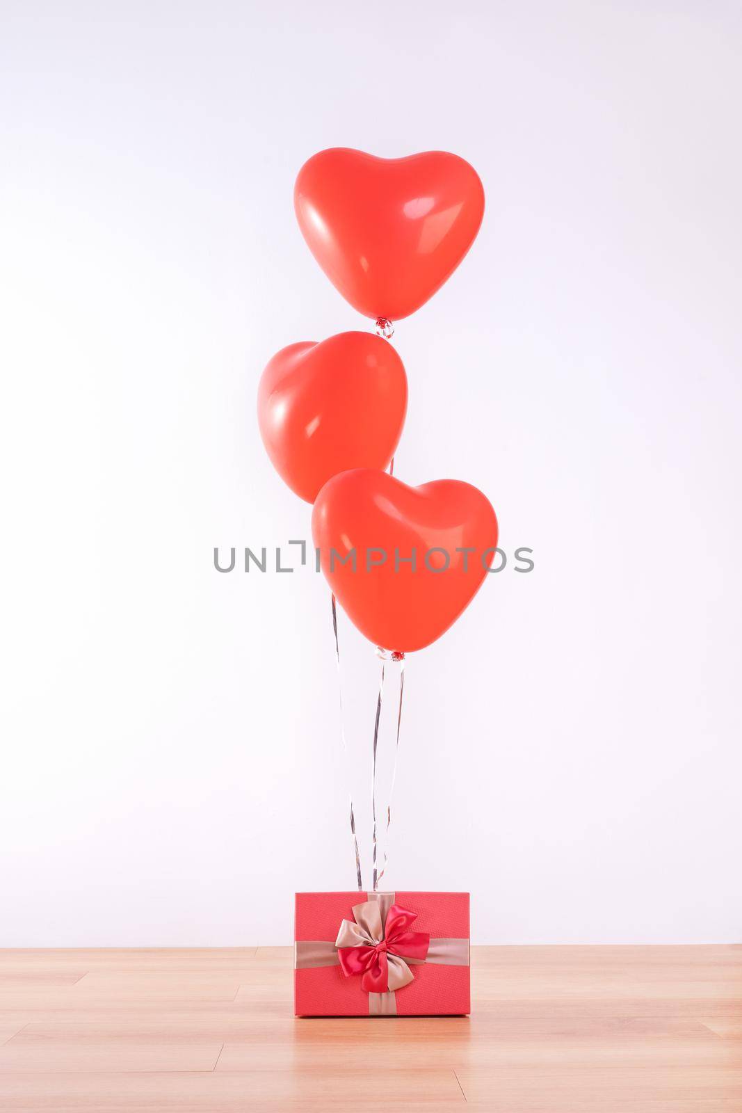 Valentine's day, Mother's day, birthday design concept - Heart helium balloon with gift box on a light wood floor, white wall background, close up.