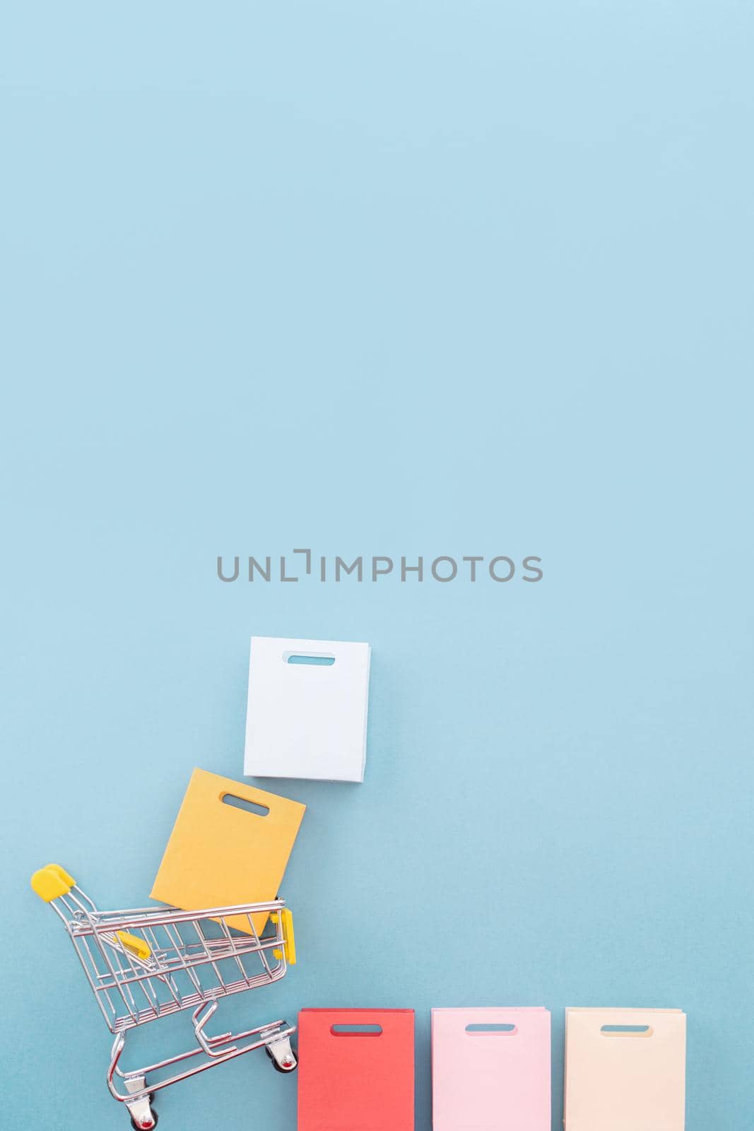 Abstract design element, annual sale, shopping season concept, mini yellow cart with colorful paper bag on pastel blue background, top view, flat lay by ROMIXIMAGE