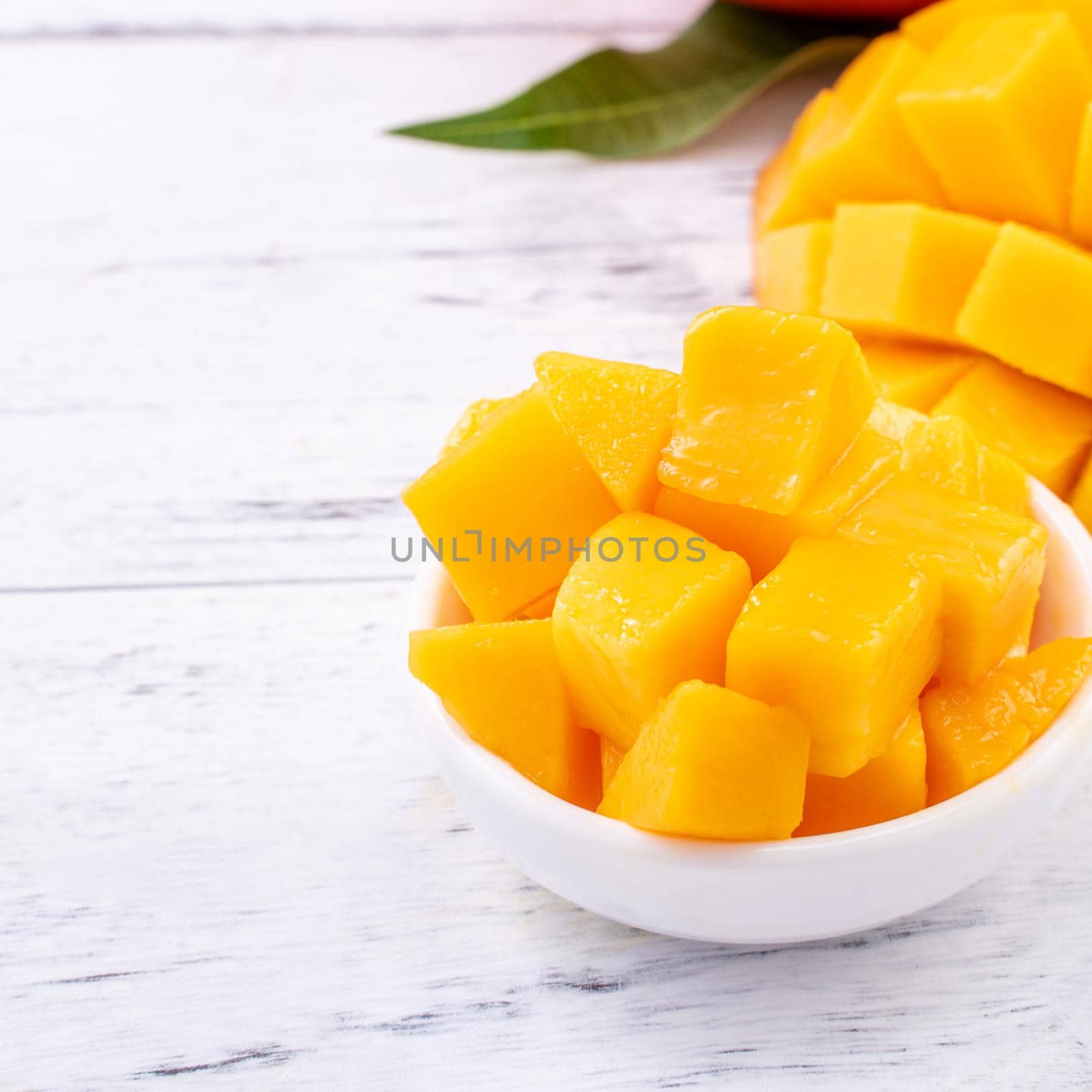 Fresh mango,beautiful chopped fruit with green leaves on bright wooden table background. Tropical fruit design concept, close up, copy space.