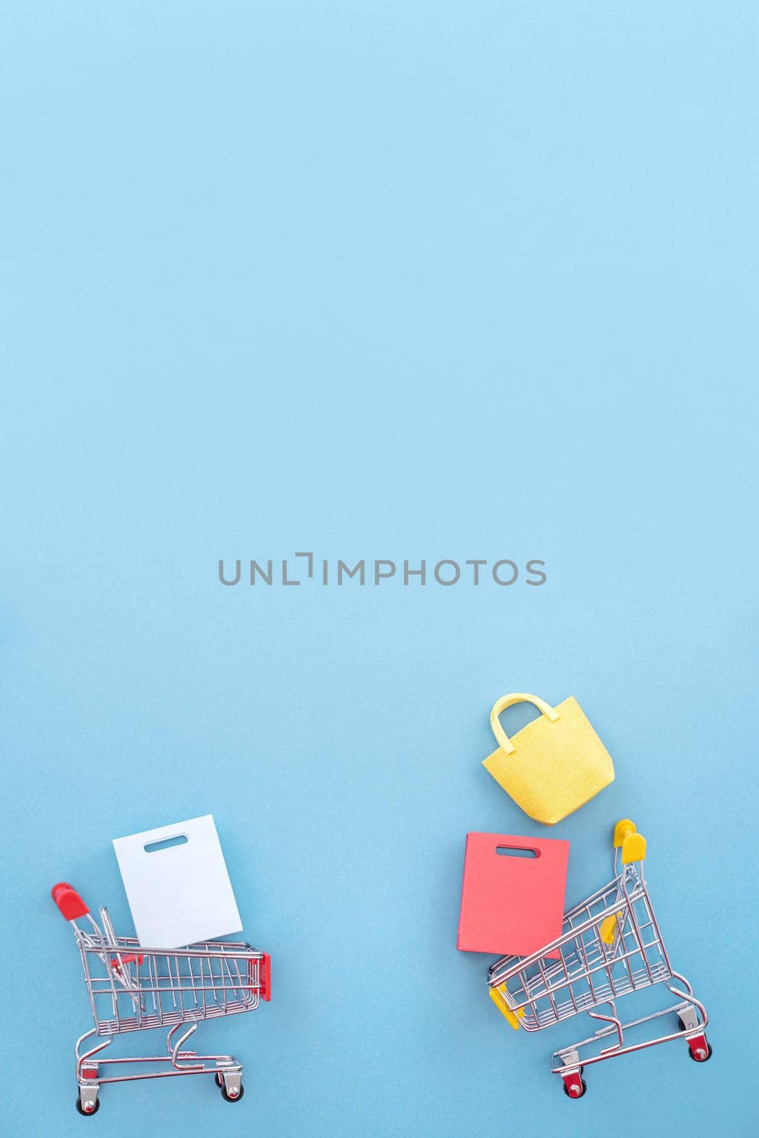Abstract design element, annual sale, shopping season concept, mini yellow cart with colorful paper bag on pastel blue background, top view, flat lay by ROMIXIMAGE