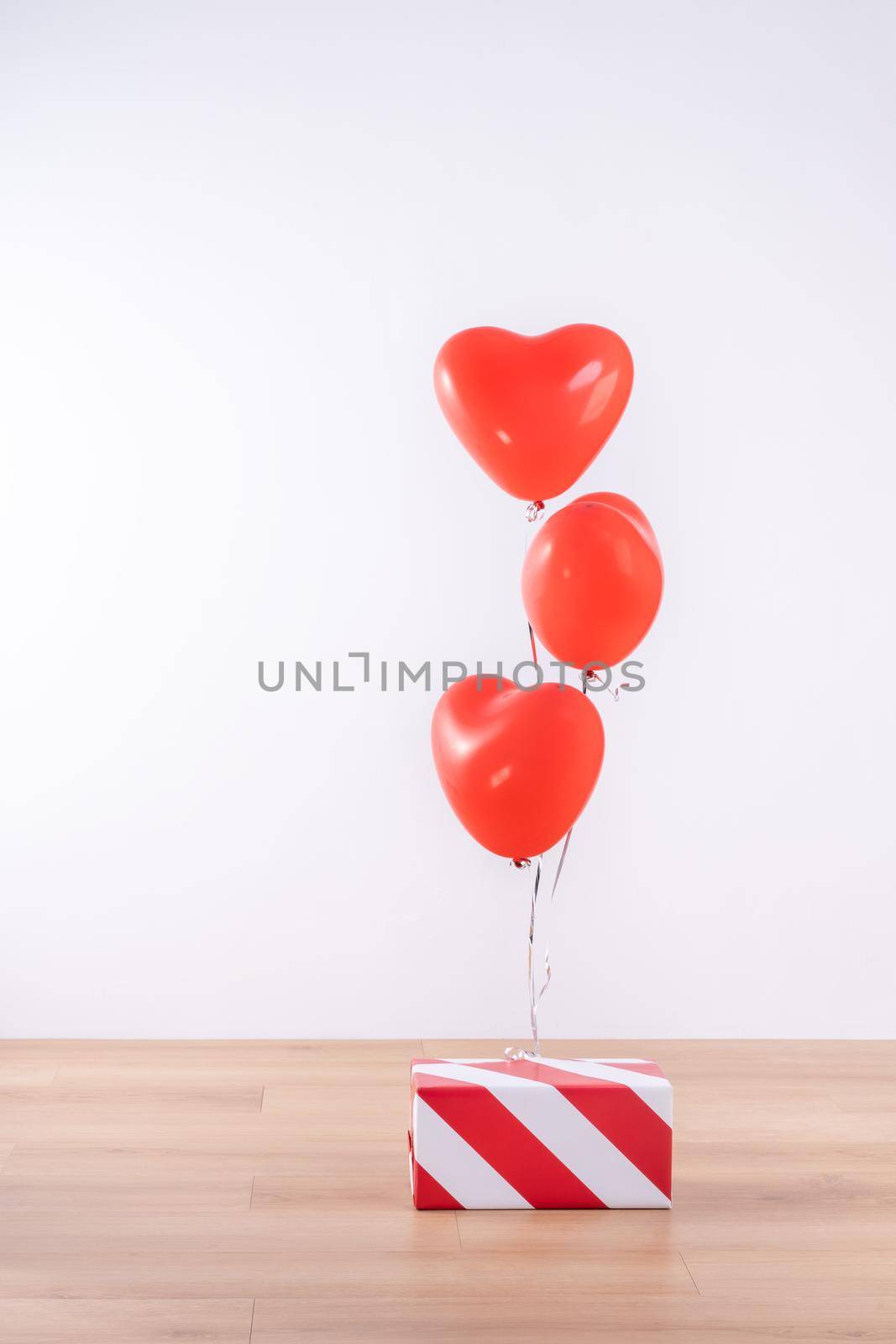 Valentine's day, Mother's day, birthday design concept - Heart helium balloon with gift box on a light wood floor, white wall background, close up. by ROMIXIMAGE