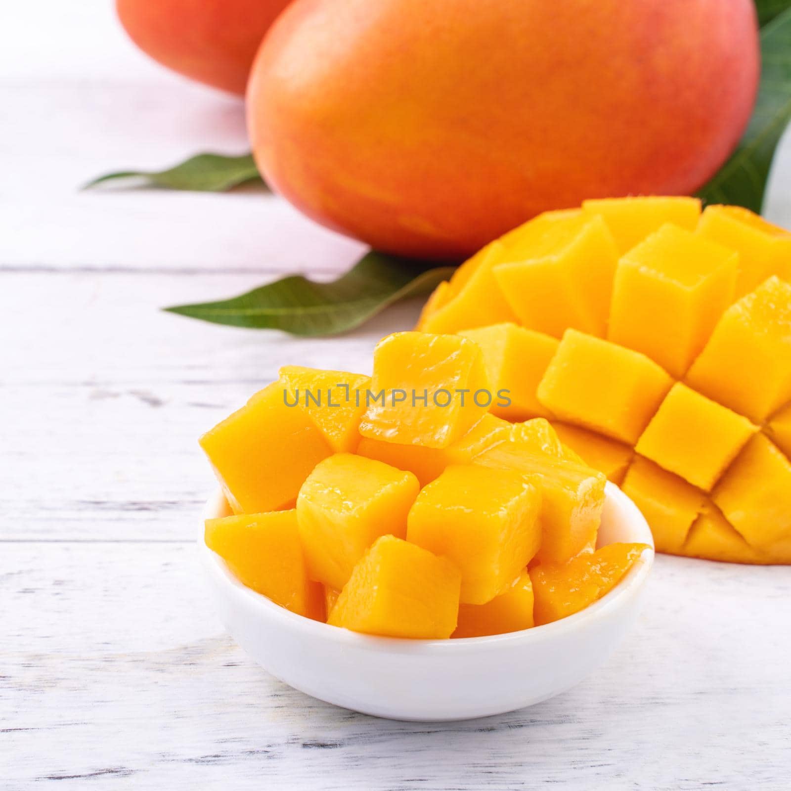 Fresh mango,beautiful chopped fruit with green leaves on bright wooden table background. Tropical fruit design concept, close up, copy space.