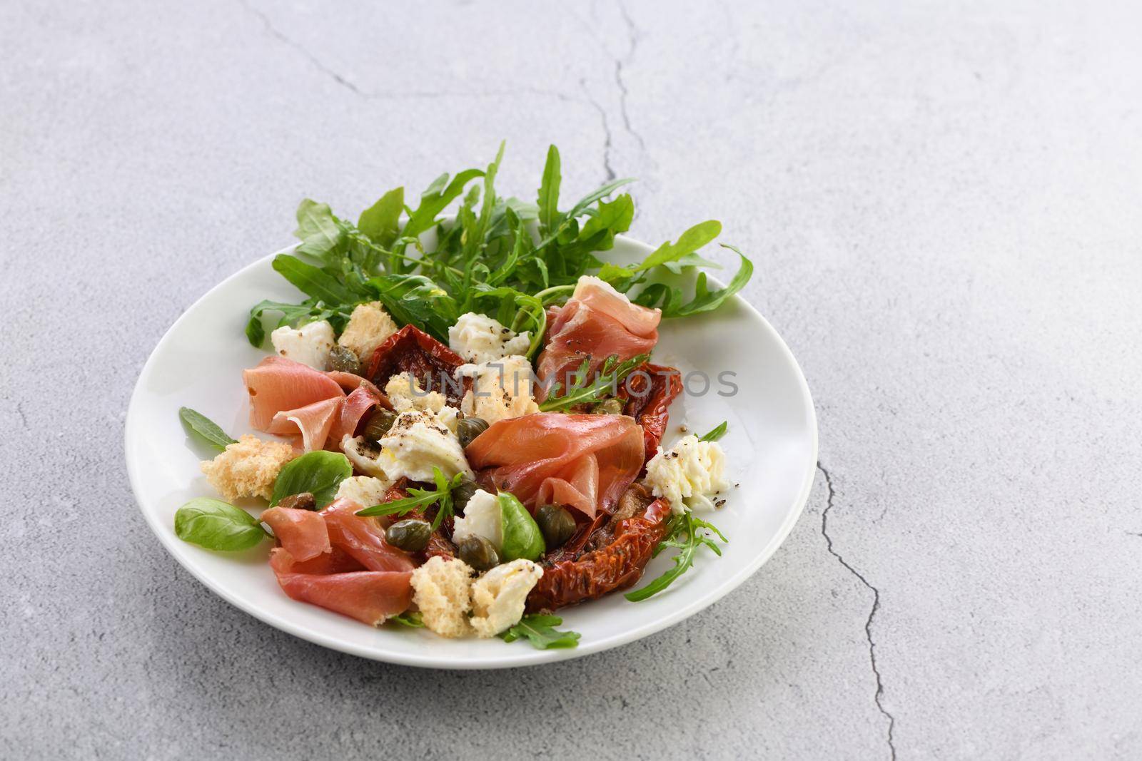 Salad arugula, Parma ham with sun-dried tomatoes, mozzarella slices, croutons, capers, seasoned oil and spices