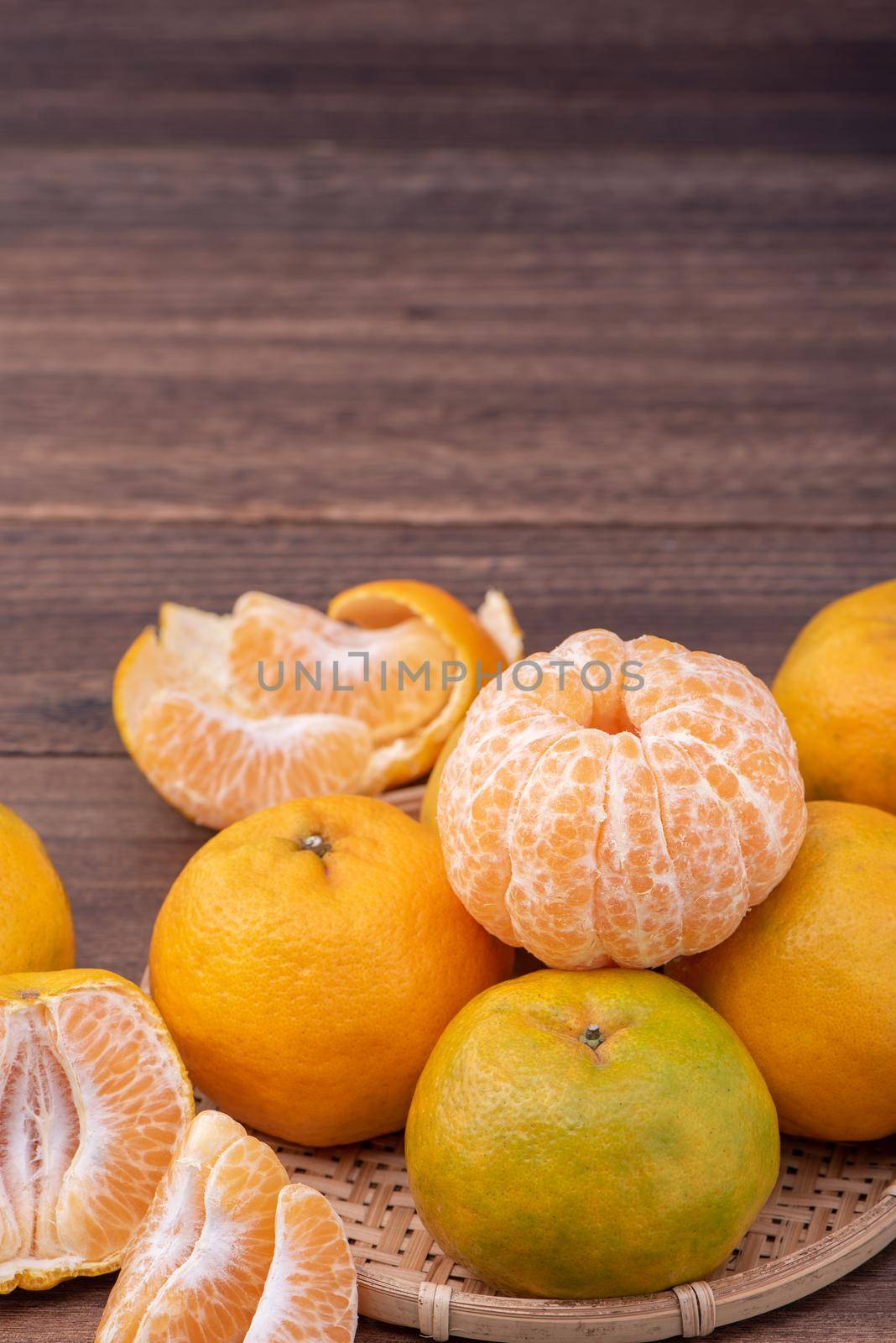 Fresh, beautiful orange color tangerine on bamboo sieve over dark wooden table. Seasonal, traditional fruit of Chinese lunar new year, close up.