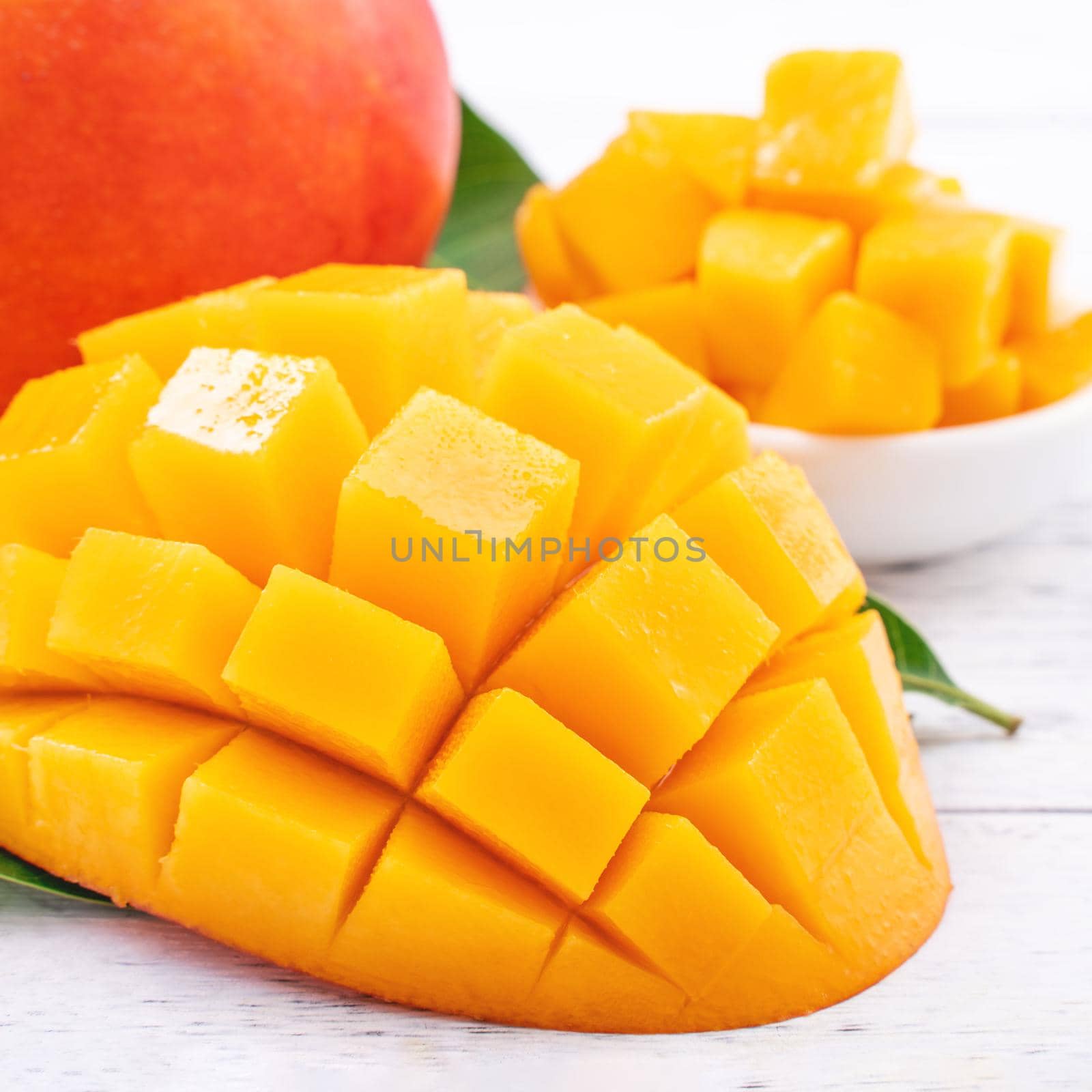 Fresh mango,beautiful chopped fruit with green leaves on bright wooden table background. Tropical fruit design concept, close up, copy space.